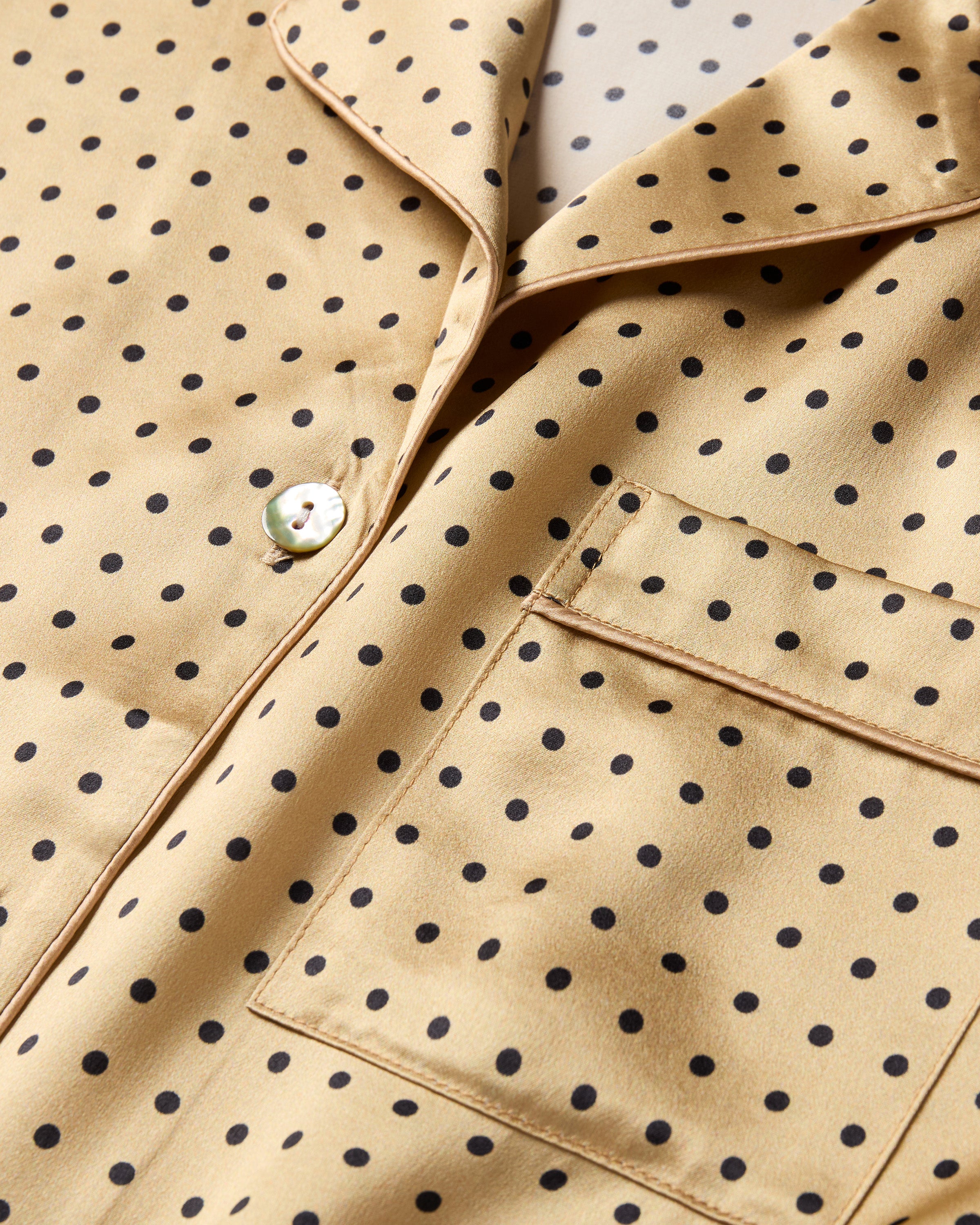 The Women's Silk Pajama Set features a gold fabric with black polka dots, including a long-sleeve button-up top with chest pocket and matching drawstring pants.