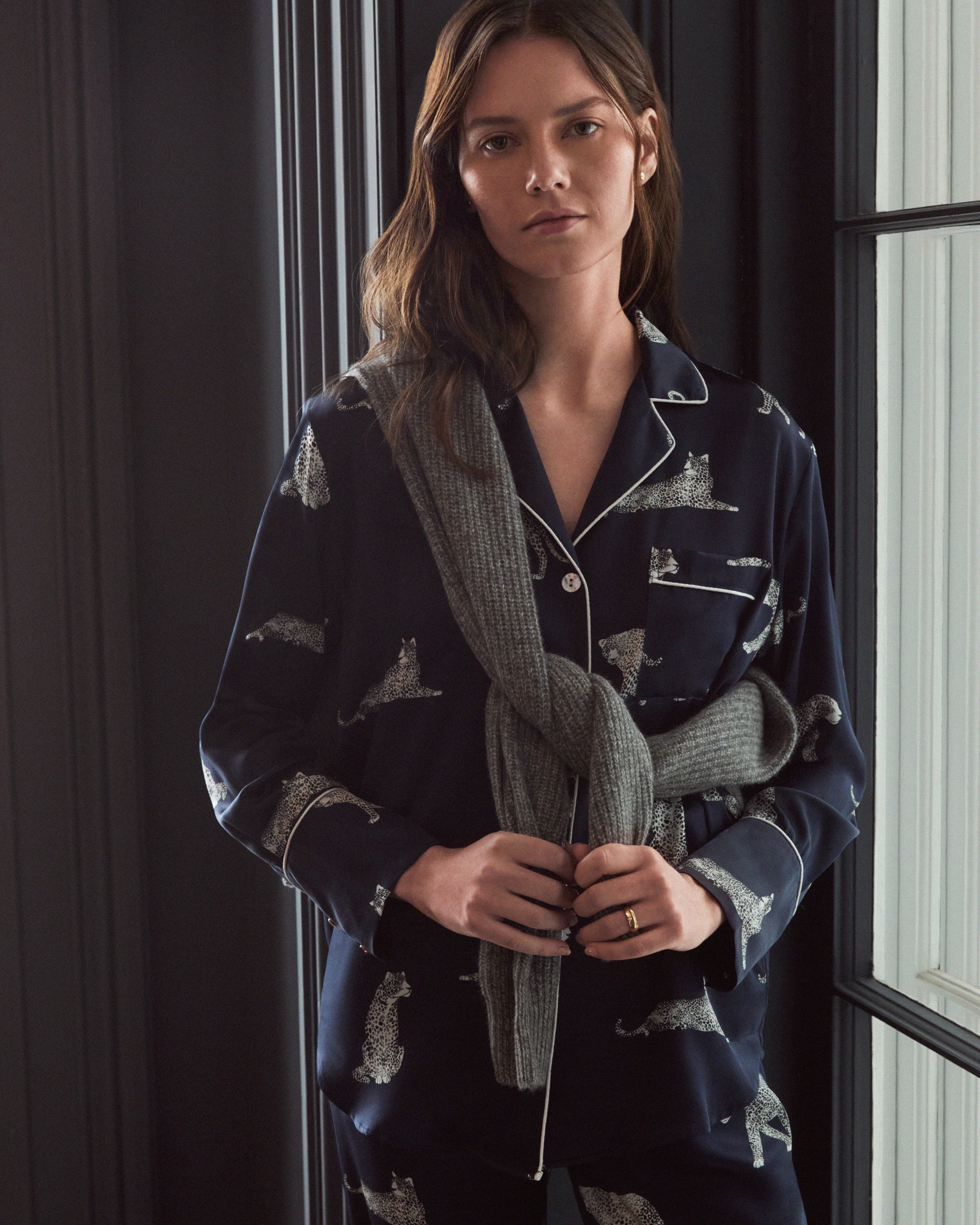 The Womens Silk Pajama Set in Panthère de Nuit by Petite Plume is navy blue with a Mulberry silk button-up shirt and pants. It features white jaguars in various poses and has white piping on the collar, cuffs, and pocket, offering elegant luxury sleepwear.