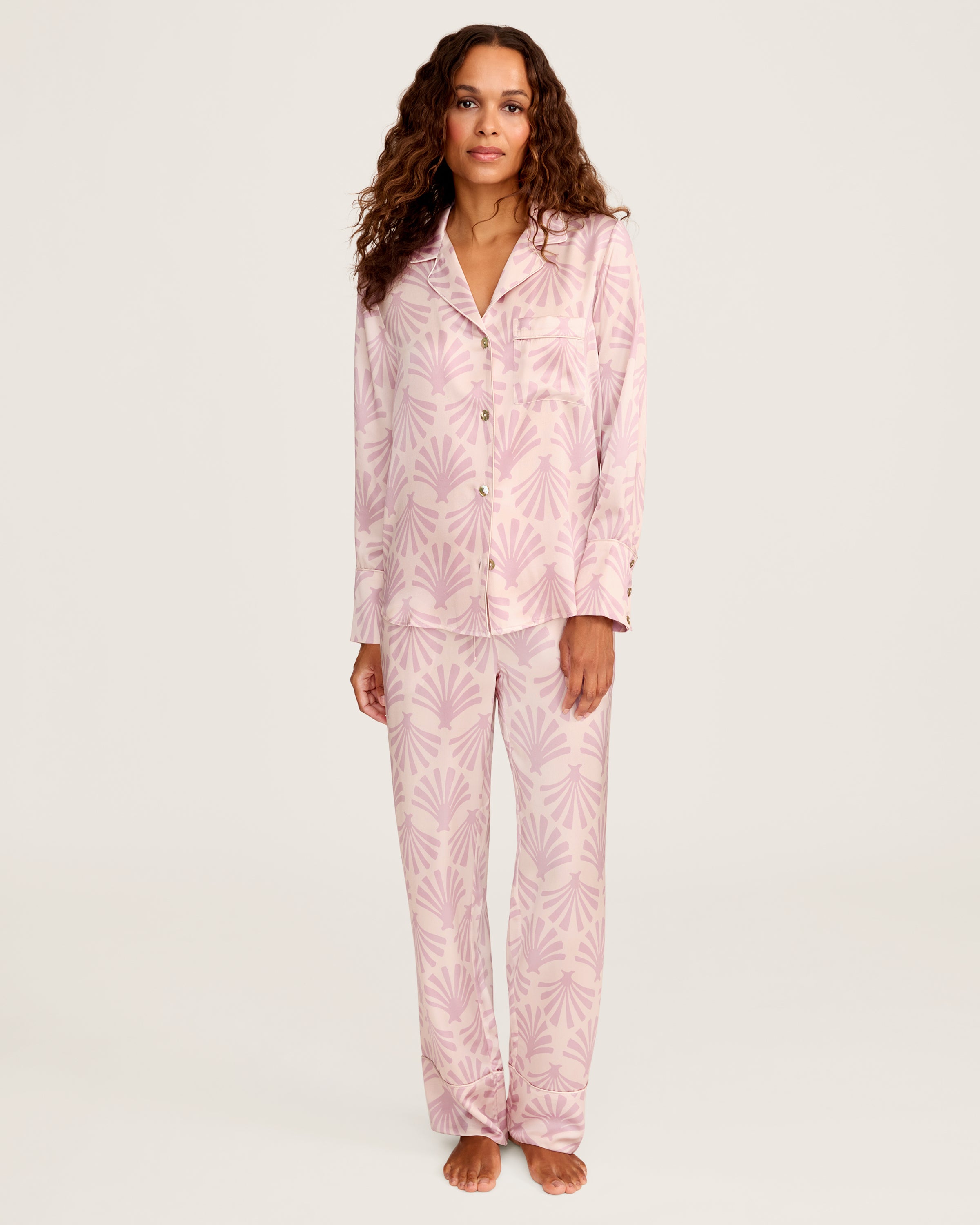 The Women's Silk Pajama Set in Blush Tide features pink long-sleeved, button-up top with collar and pocket, adorned with a blush and mauve geometric fan pattern, shown flat with matching pants beside the top.