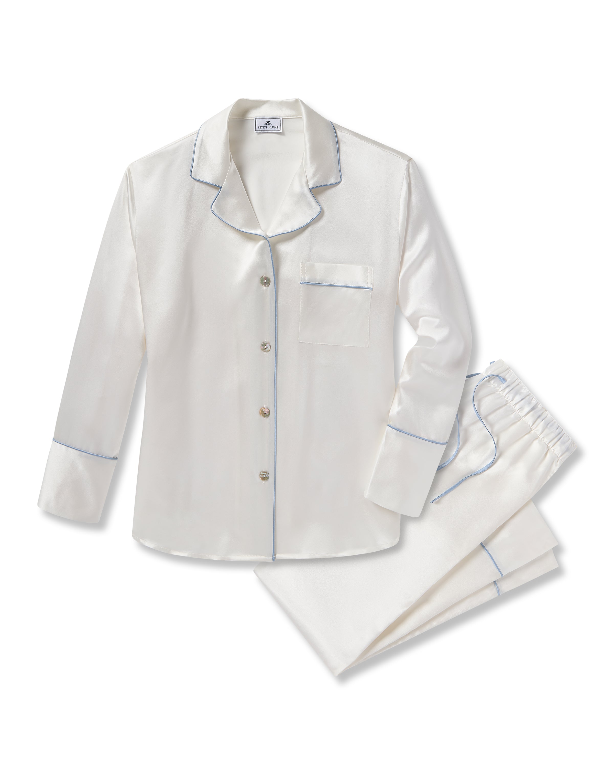The Petite Plume Womens Silk Pajama Set, in white with periwinkle piping, includes a silky top with long sleeves, buttons, a notched collar, and chest pocket. The pants have an elastic waistband. Ideal as a bridal keepsake, they are elegantly arranged on a solid white background.