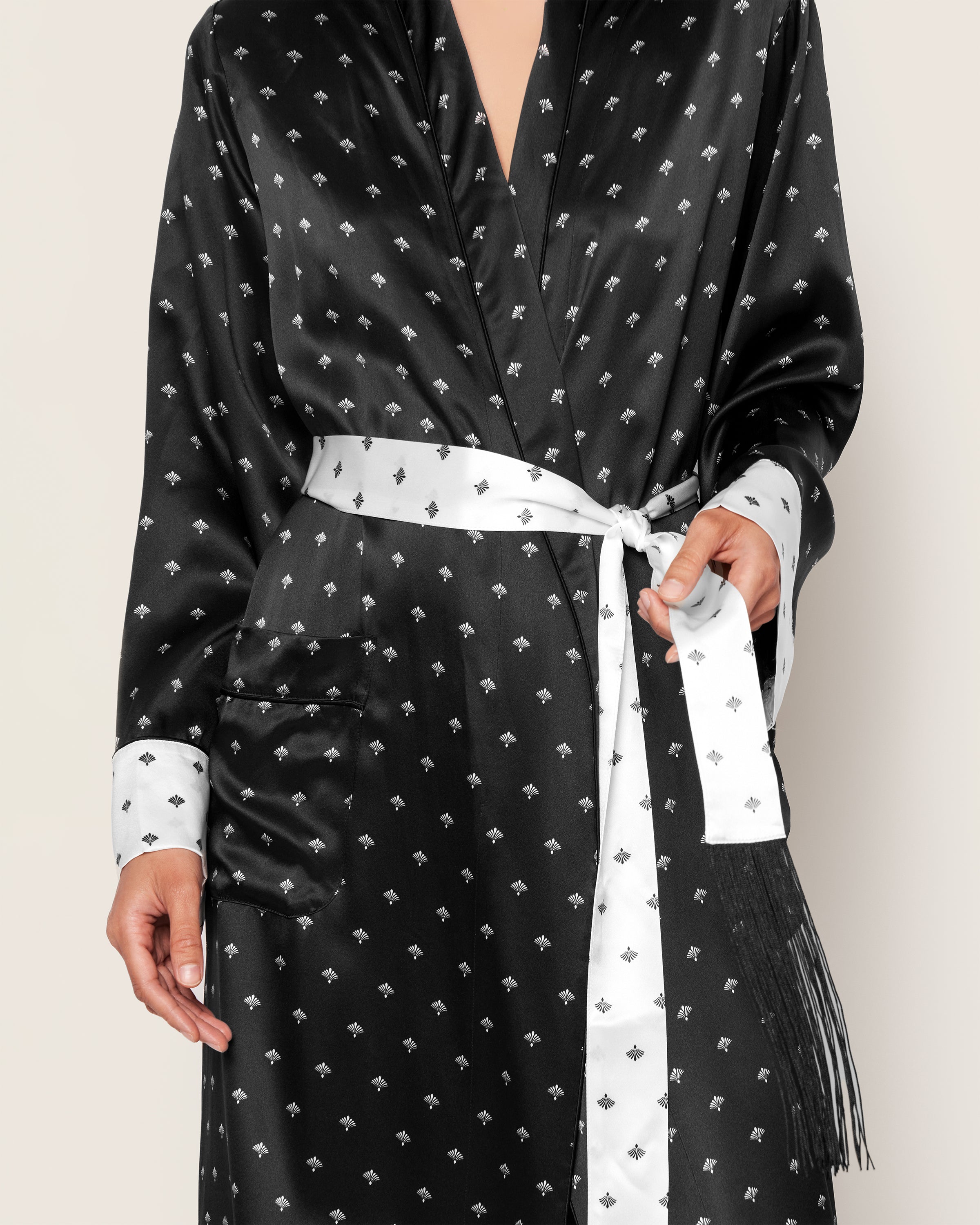 A person models the Petite Plume Womens Silk Long Robe in Black Art Nouveau. It features a fan motif, white cuffs, and a front-tied white belt. The robe, with its pocket detail, rests against an off-white background.
