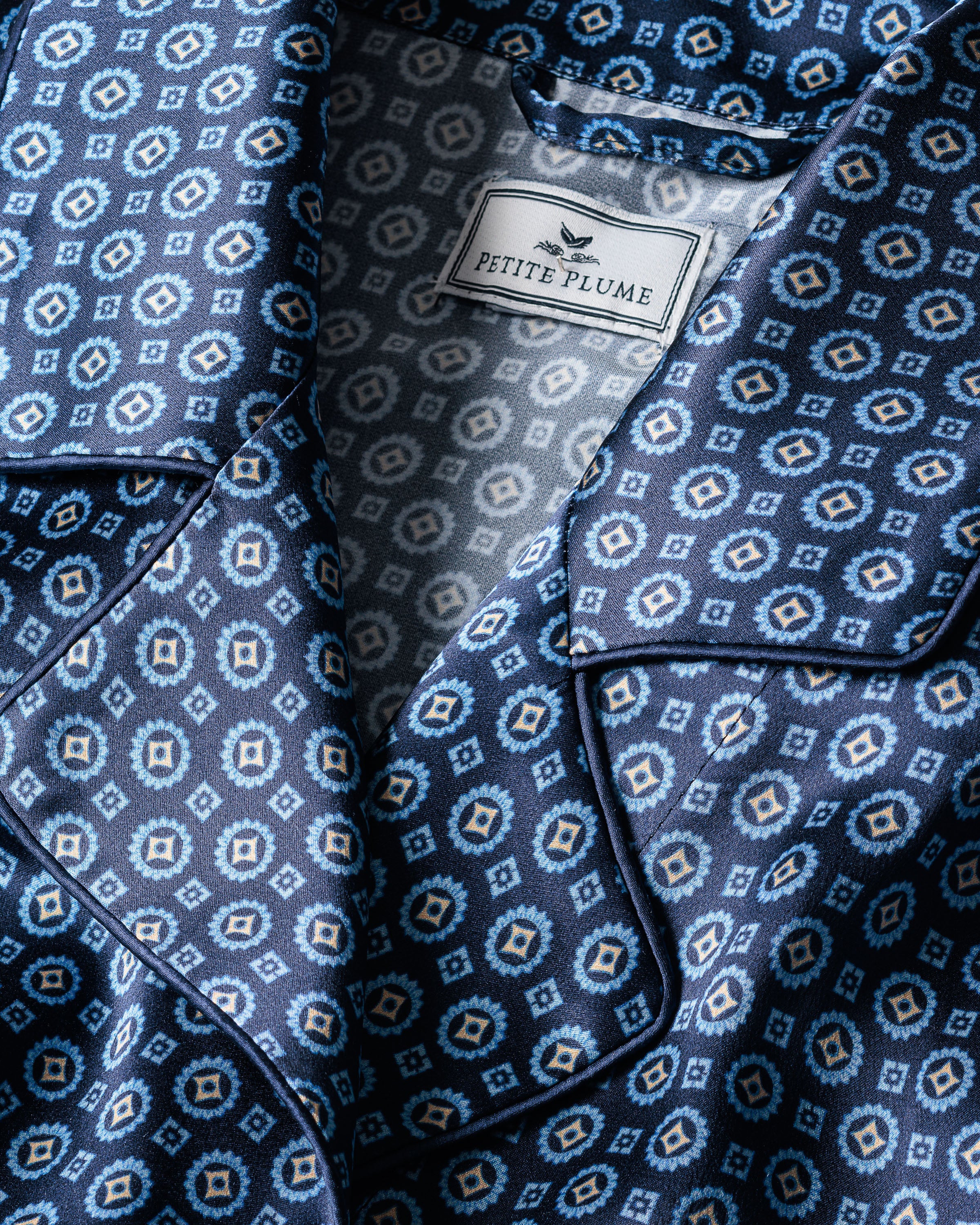Close-up of the Womens Silk Robe in Midnight Foulard with geometric designs by Petite Plume. The stitching and silky material, similar to fine Mulberry silk, create a textured appearance. Ideal for luxurious sleepwear, it features an elegant collar and button detail.