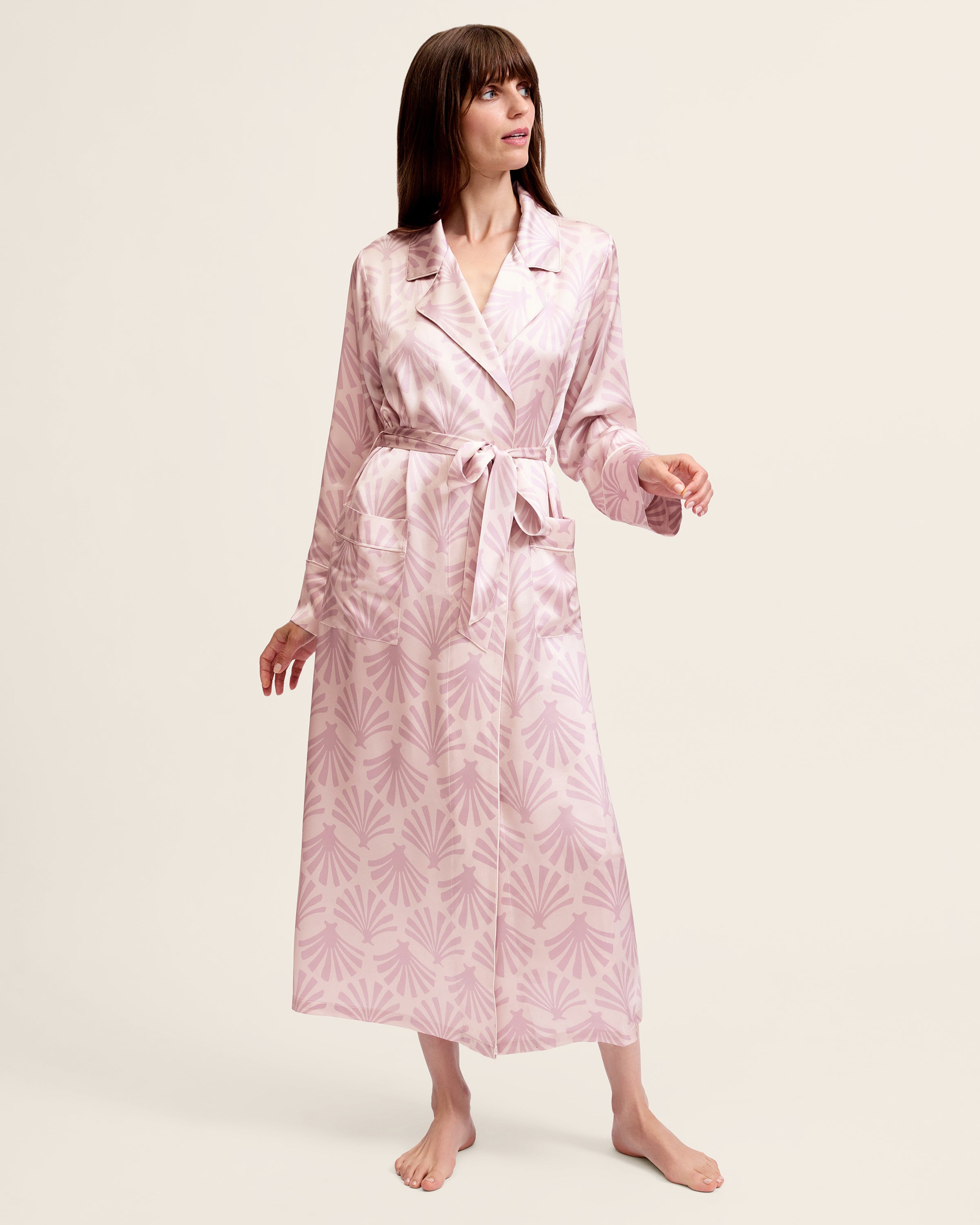 The Women's Silk Robe in Blush Tide features a light pink hue with a darker pink geometric pattern, notched collar, long sleeves, and a matching waist belt.