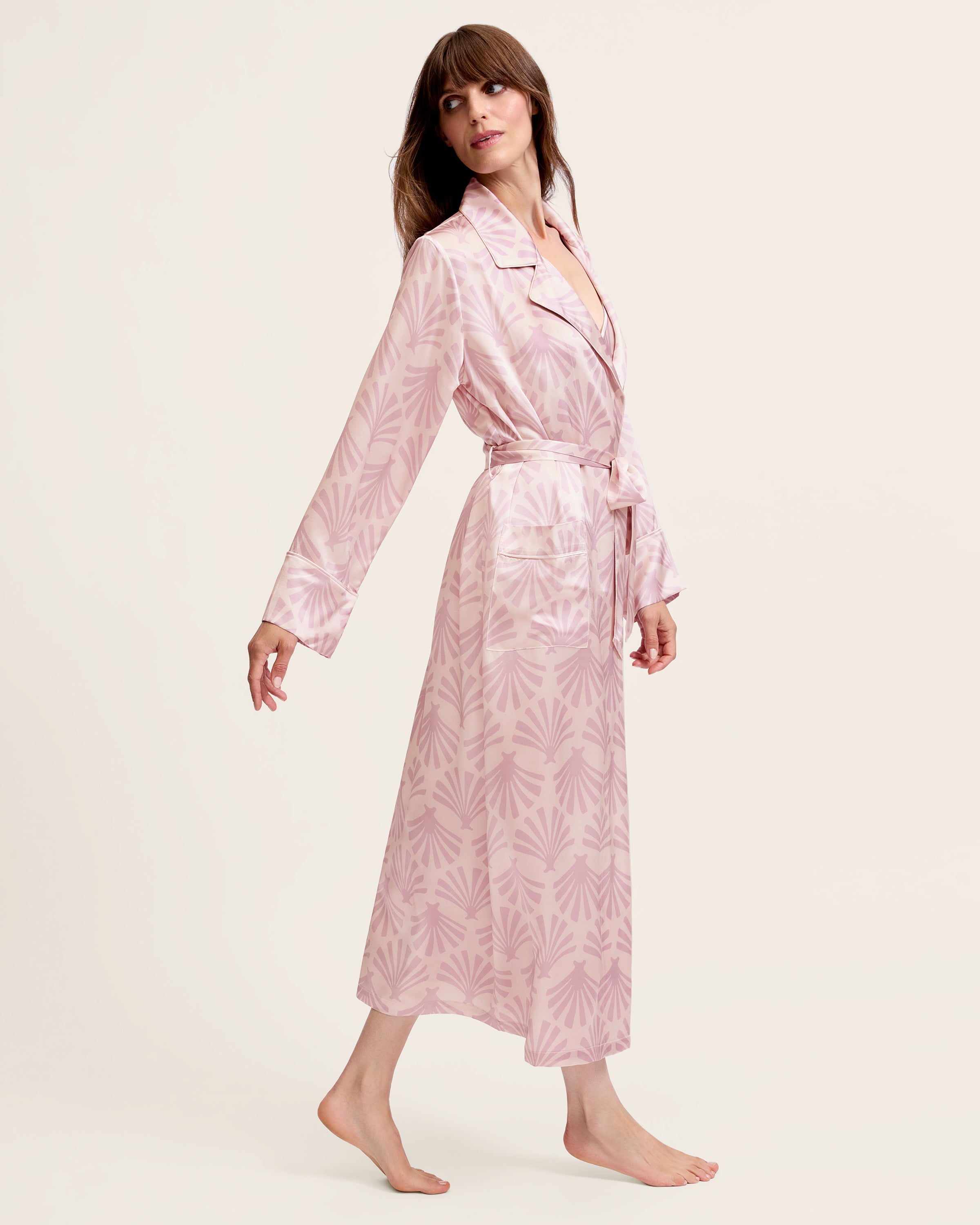 The Women's Silk Robe in Blush Tide features a light pink hue with a darker pink geometric pattern, notched collar, long sleeves, and a matching waist belt.