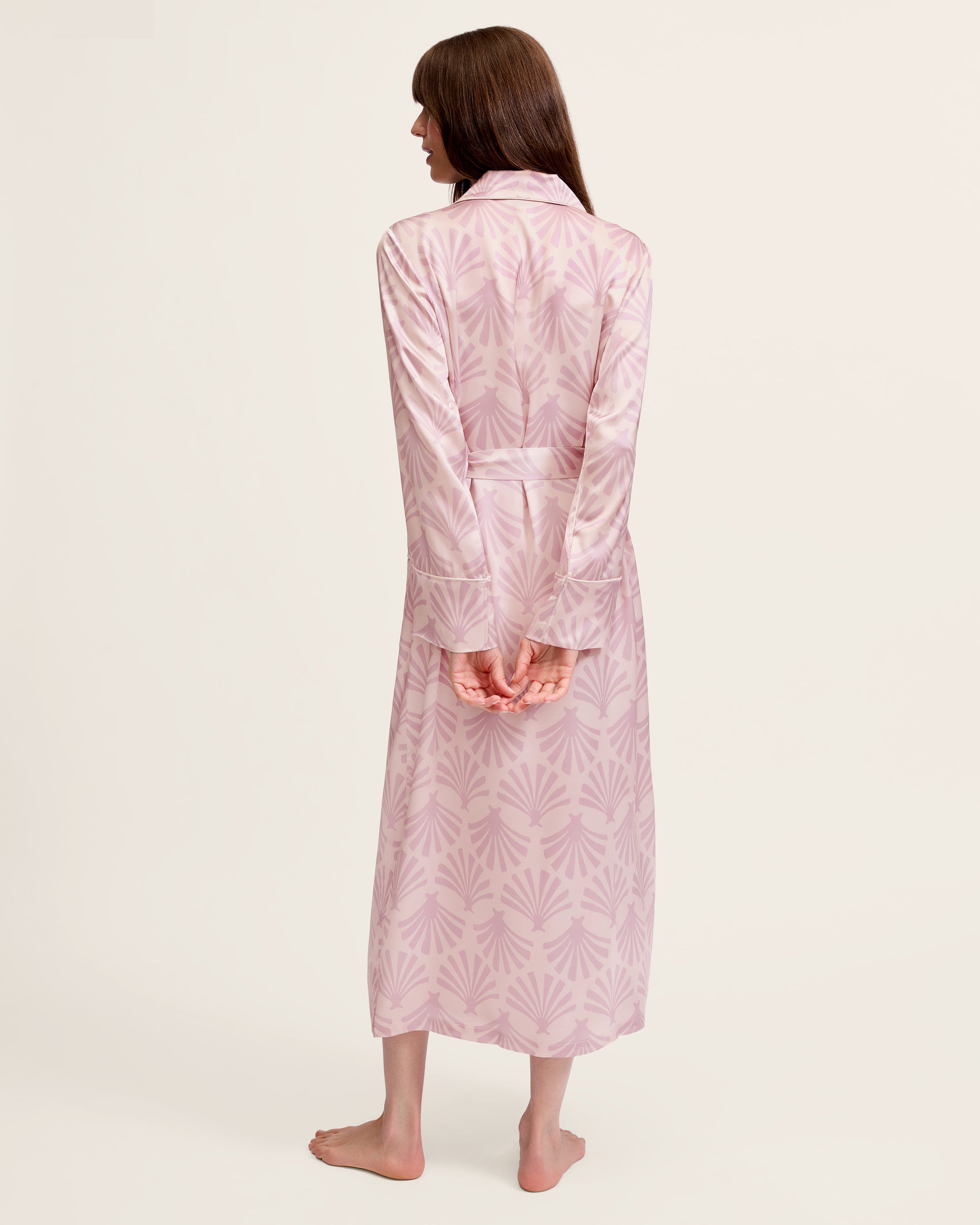 The Women's Silk Robe in Blush Tide features a light pink hue with a darker pink geometric pattern, notched collar, long sleeves, and a matching waist belt.