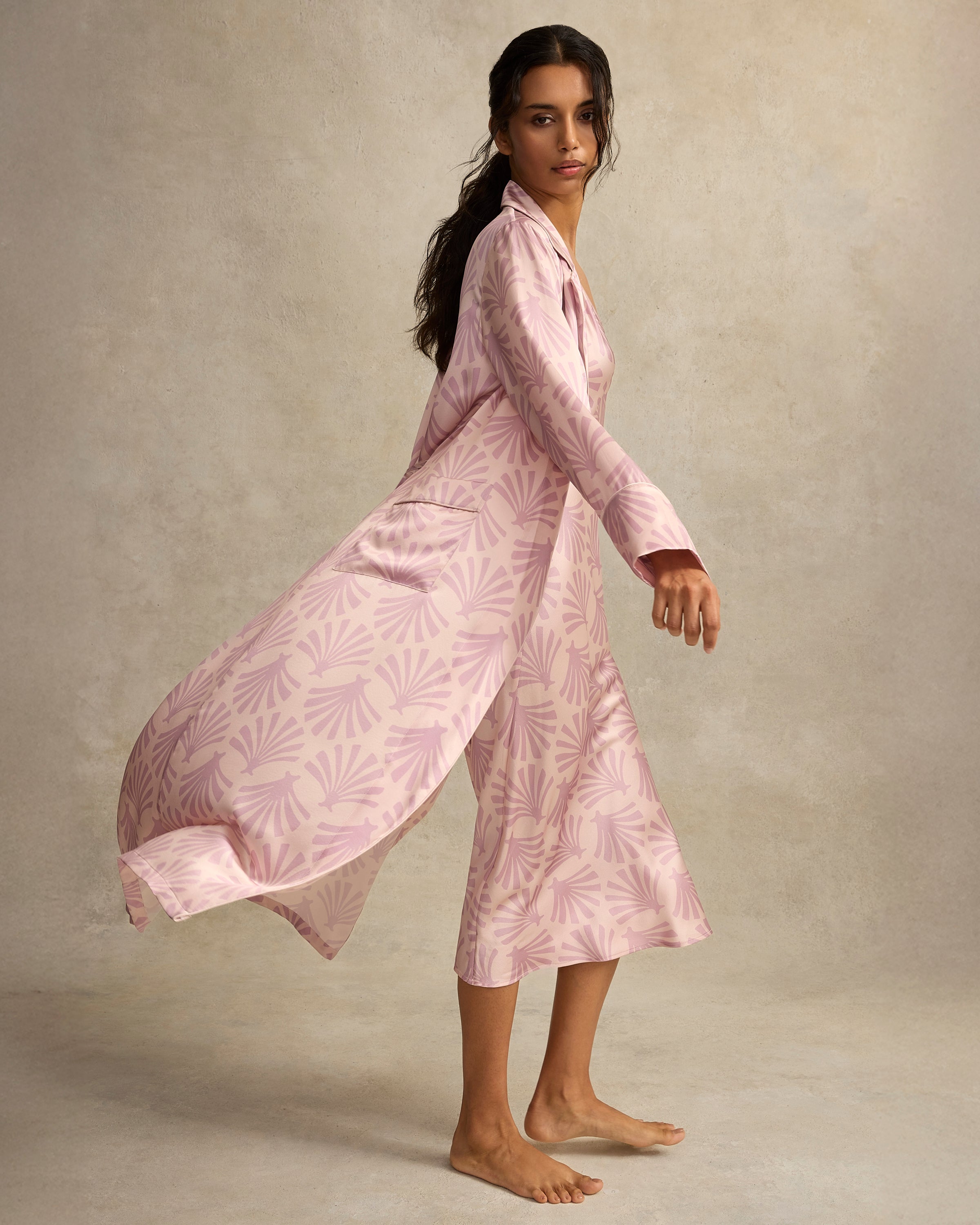 The Women's Silk Robe in Blush Tide features a light pink hue with a darker pink geometric pattern, notched collar, long sleeves, and a matching waist belt.