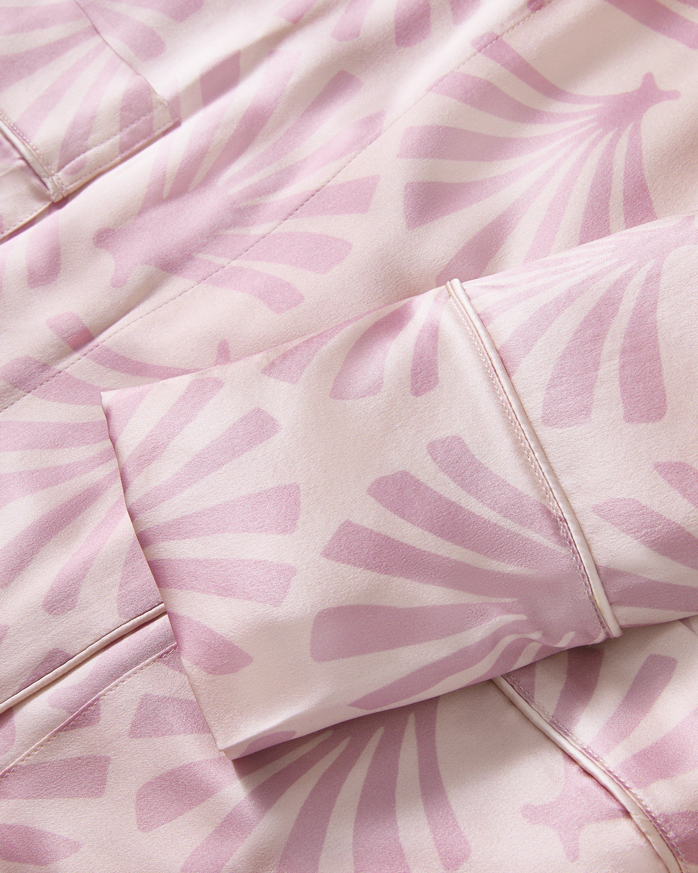 The Women's Silk Robe in Blush Tide features a light pink hue with a darker pink geometric pattern, notched collar, long sleeves, and a matching waist belt.