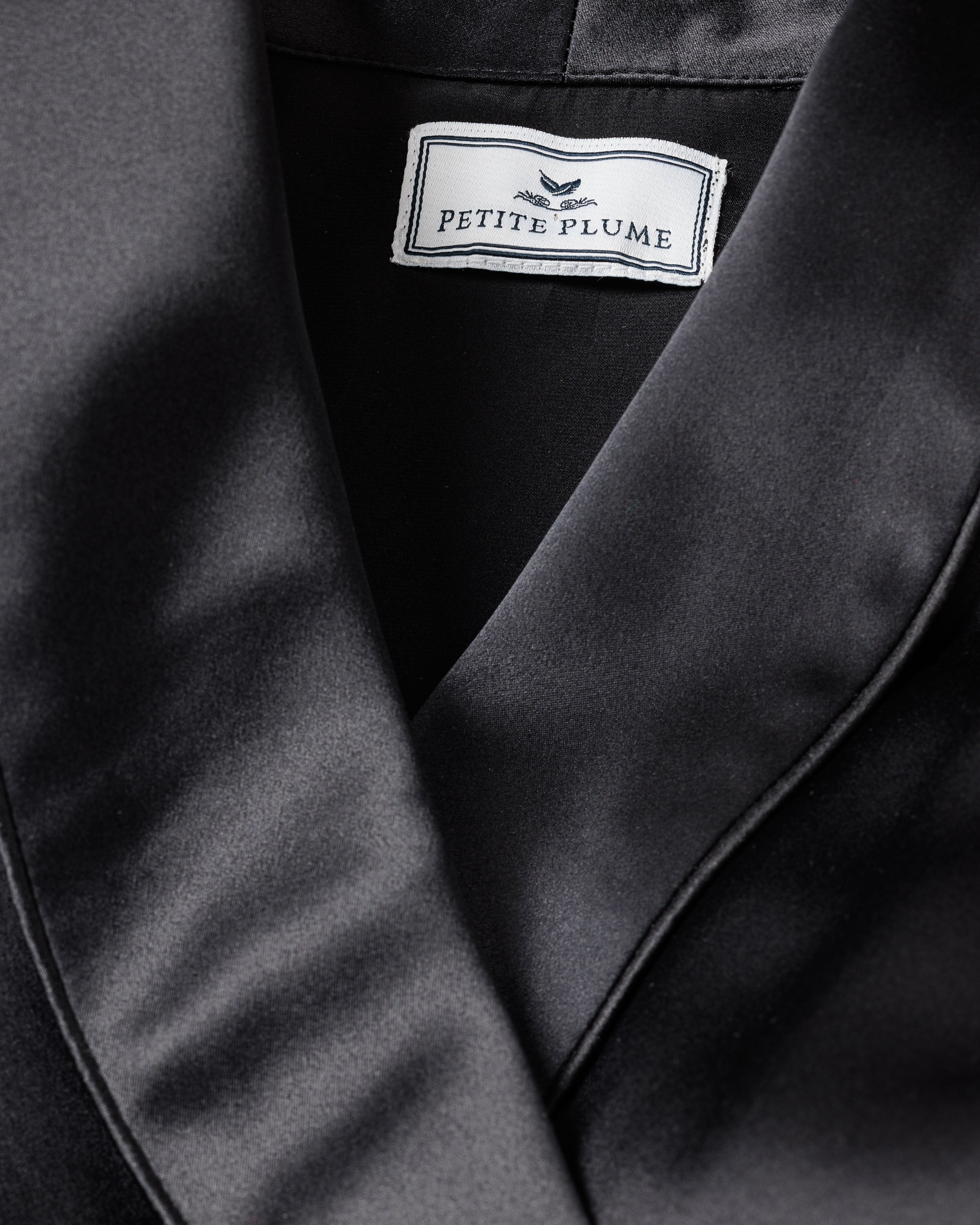 Close-up of a Womens Silk Short Robe in Black by Petite Plume, showcasing its luxurious hypoallergenic Mulberry Silk with a smooth, glossy texture ideal for sleepwear.