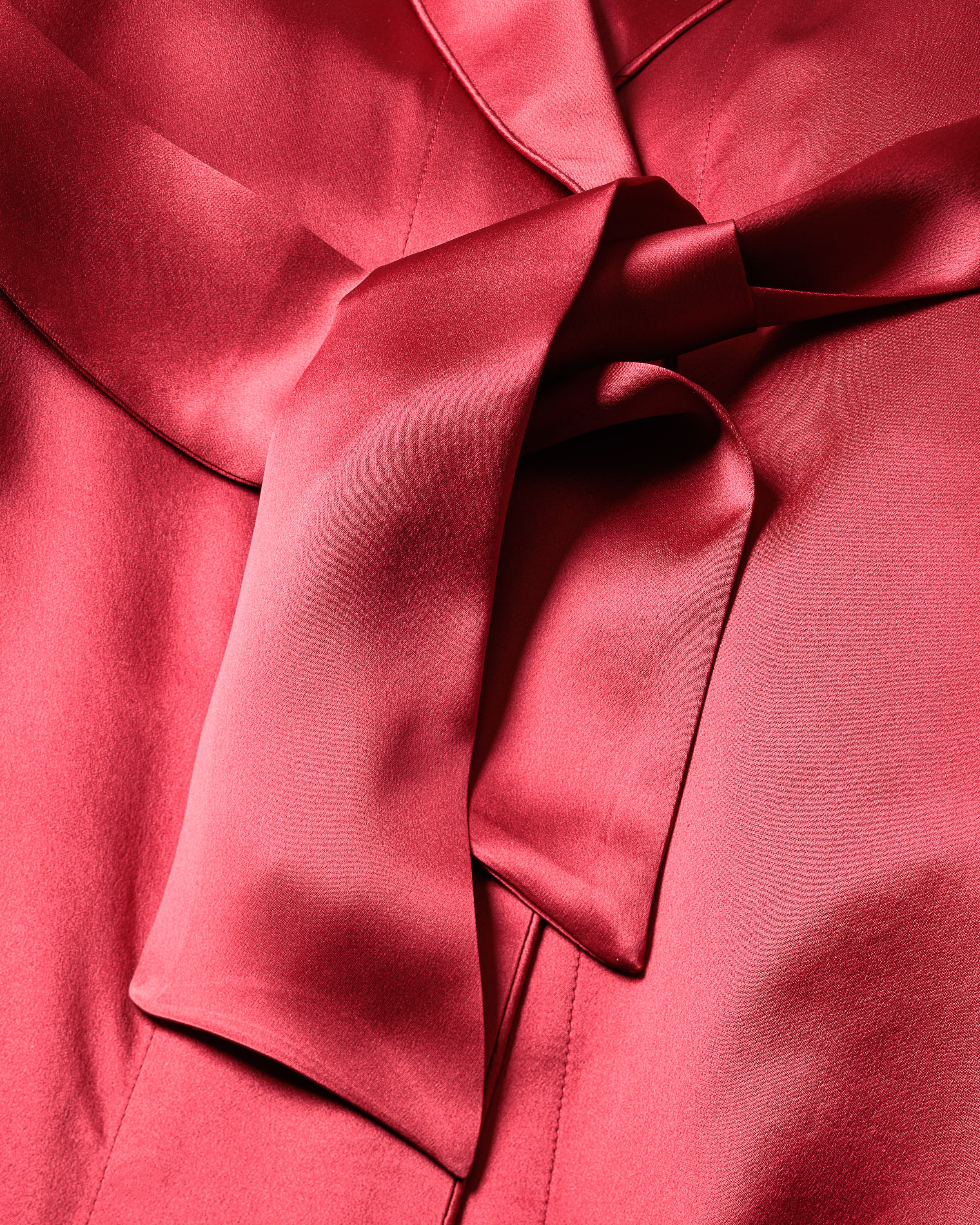 Close-up of Petite Plumes Womens Silk Short Robe in Crimson made from Mulberry Silk, showcasing a prominent tied bow. The smooth texture and subtle sheen enhance its luxury and elegance, providing a hypoallergenic experience.