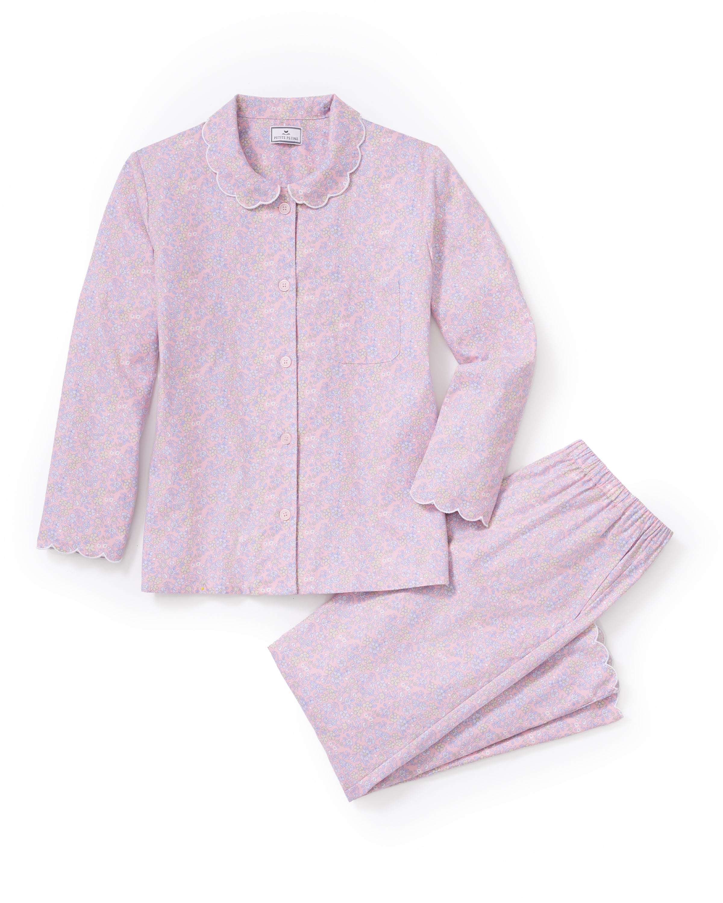A woman stands barefoot against a plain background, wearing the Women's Twill Colette Pajama Set in Fleur Blush—a matching long-sleeve, button-up top and pants with a light purple and pink floral pattern.