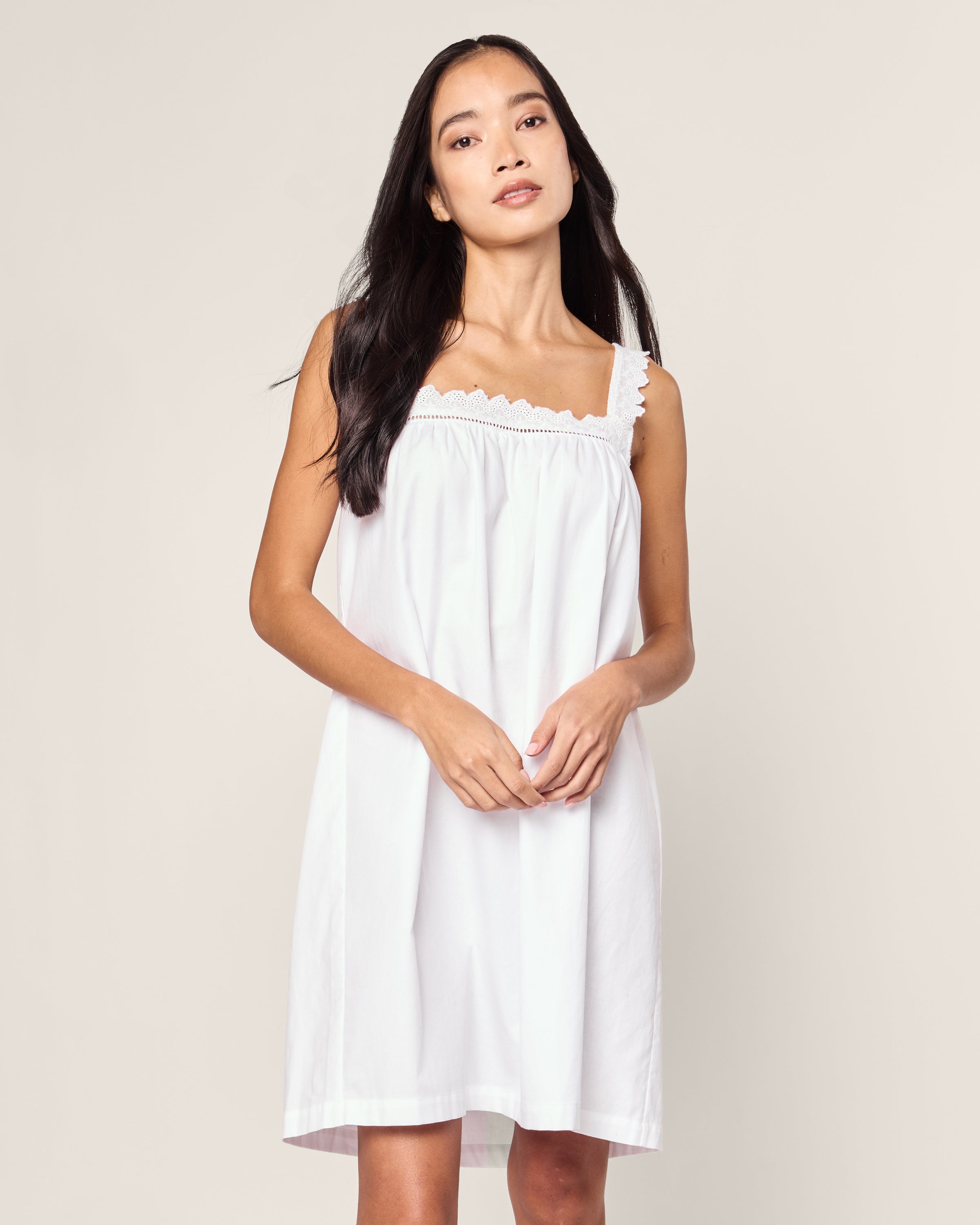 A woman with long dark hair stands against a neutral background wearing the luxurious Womens Twill Esme Nightgown in White by Petite Plume. She looks slightly upward with a neutral expression, holding her hands loosely in front.