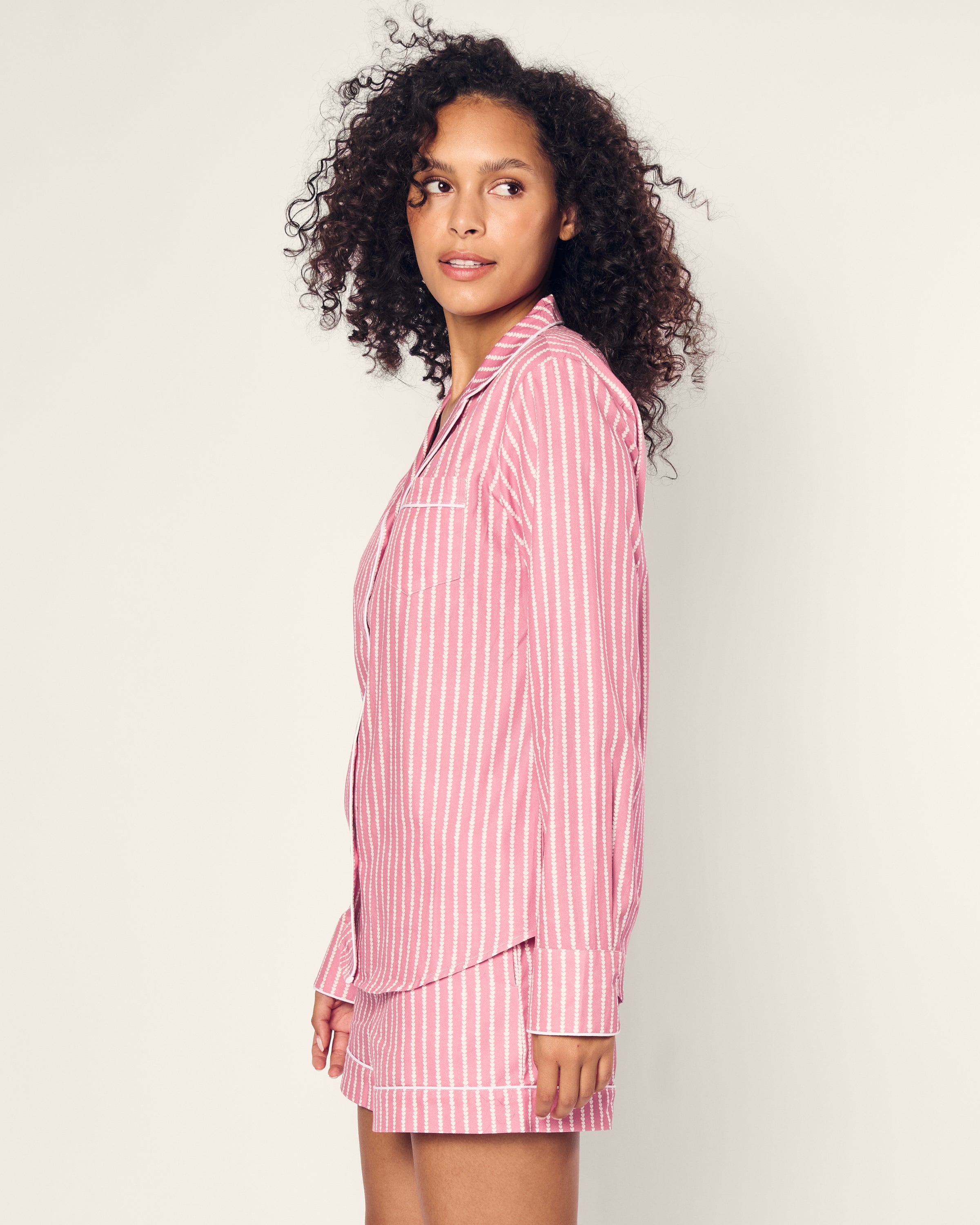 A woman with curly hair stands against a light background, wearing Petite Plumes Womens Twill Long Sleeve Short Set in Love Lines. Made from high-quality cotton, this luxurious sleepwear suits her as she gazes thoughtfully to her right.