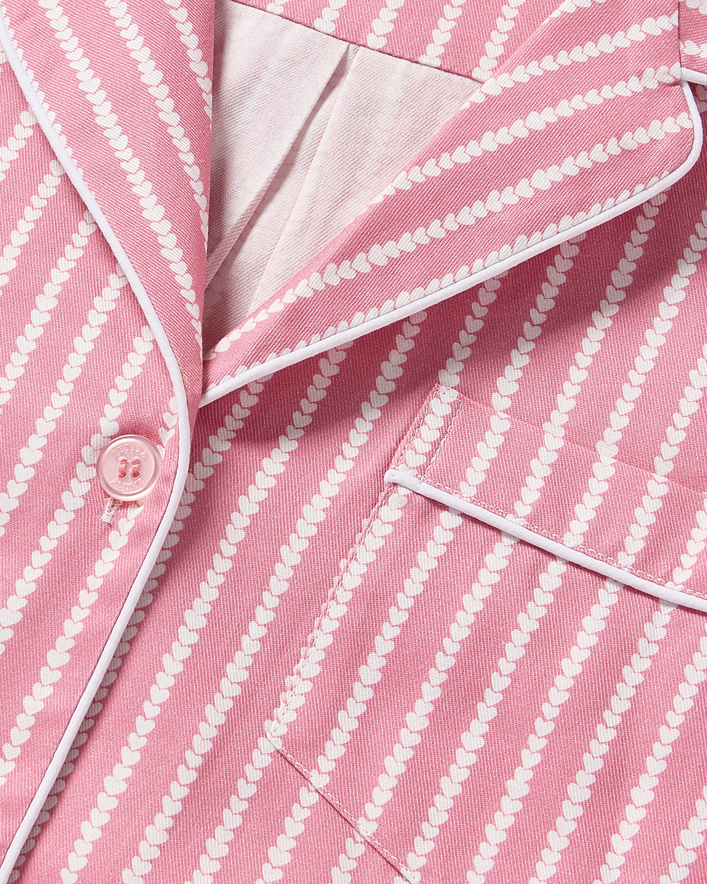 Close-up of the Womens Twill Long Sleeve Short Set in Love Lines by Petite Plume, showcasing pink and white striped pajama fabric with buttons. Crafted from high-quality cotton, it features diagonal dotted stripes and white piping along the collar and pocket edge for a luxurious touch.