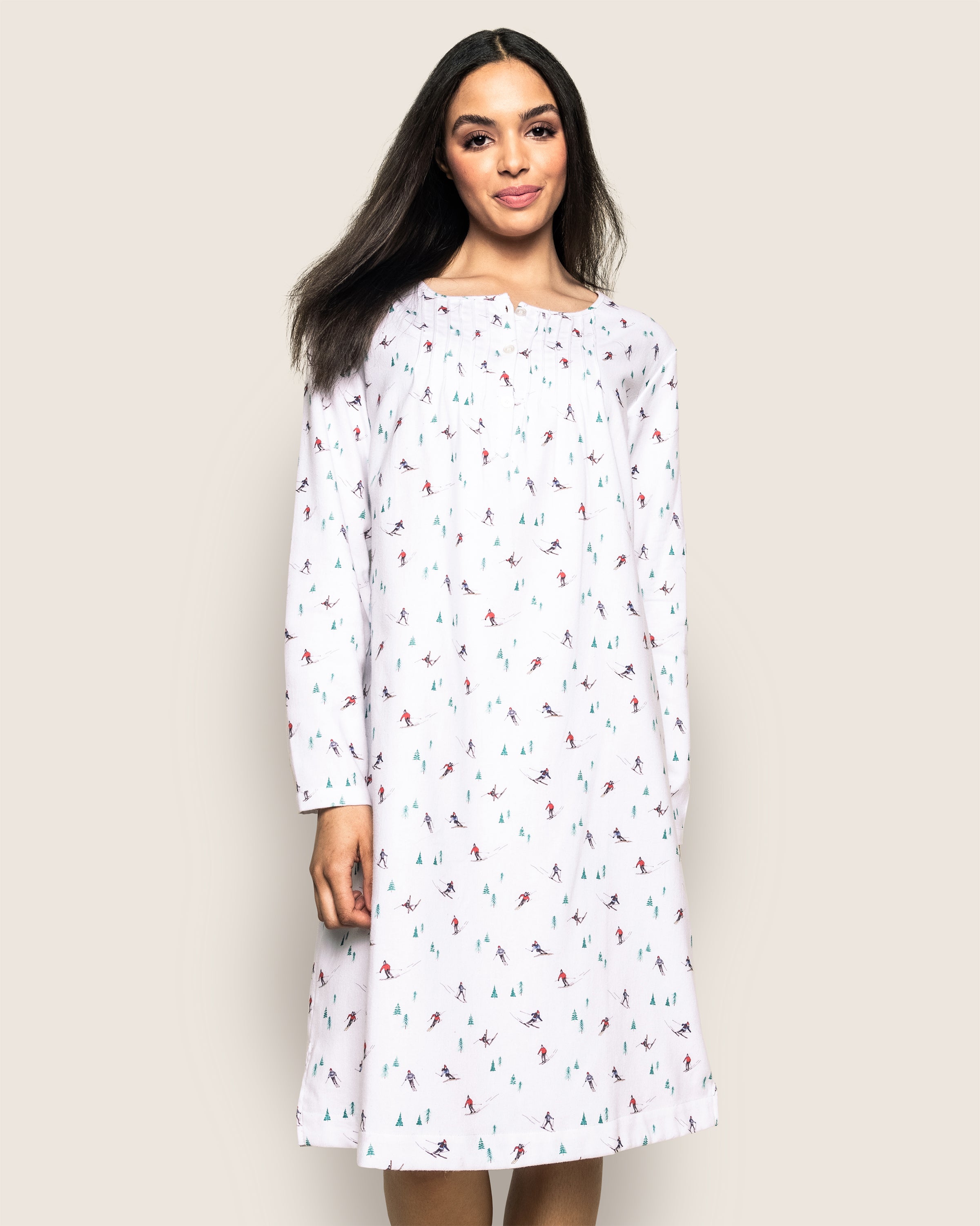 A person wearing Petite Plumes Womens Flannel Beatrice Nightgown in Après Ski with a colorful tree pattern stands against a light background, smiling.