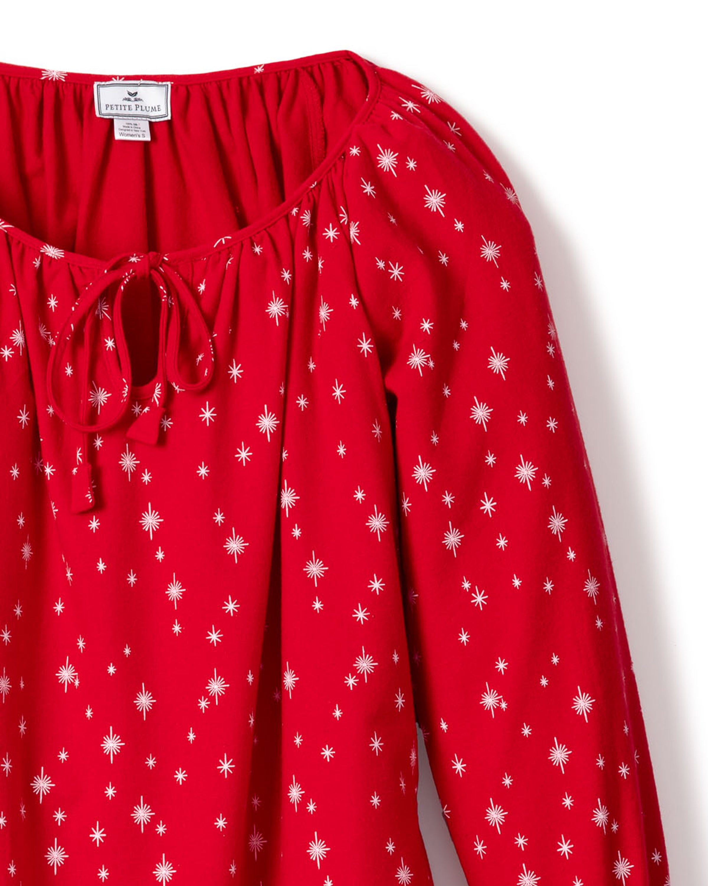 The Womens Flannel Delphine Nightgown in Starry Night by Petite Plume features a red long-sleeve design with a tie neckline and white star-like patterns on lightweight 100% cotton flannel, shown against a white background.