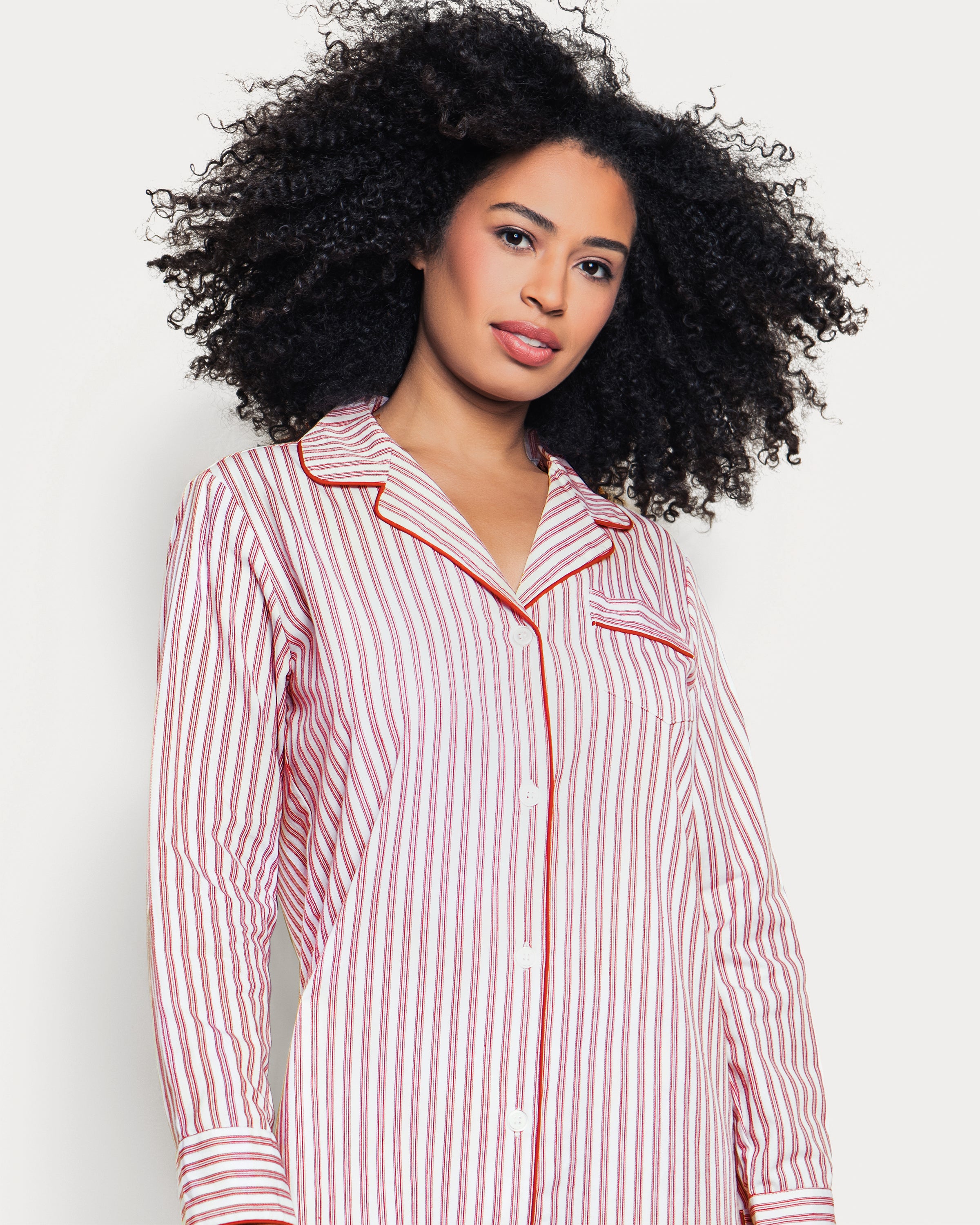 Close-up of the Womens Twill Nightshirt in Antique Red Ticking by Petite Plume, showcasing white fabric with vertical red pinstripes. Made from the finest quality cotton, it features a buttoned shirt with a notched collar and chest pocket, detailed with matching striped edges.