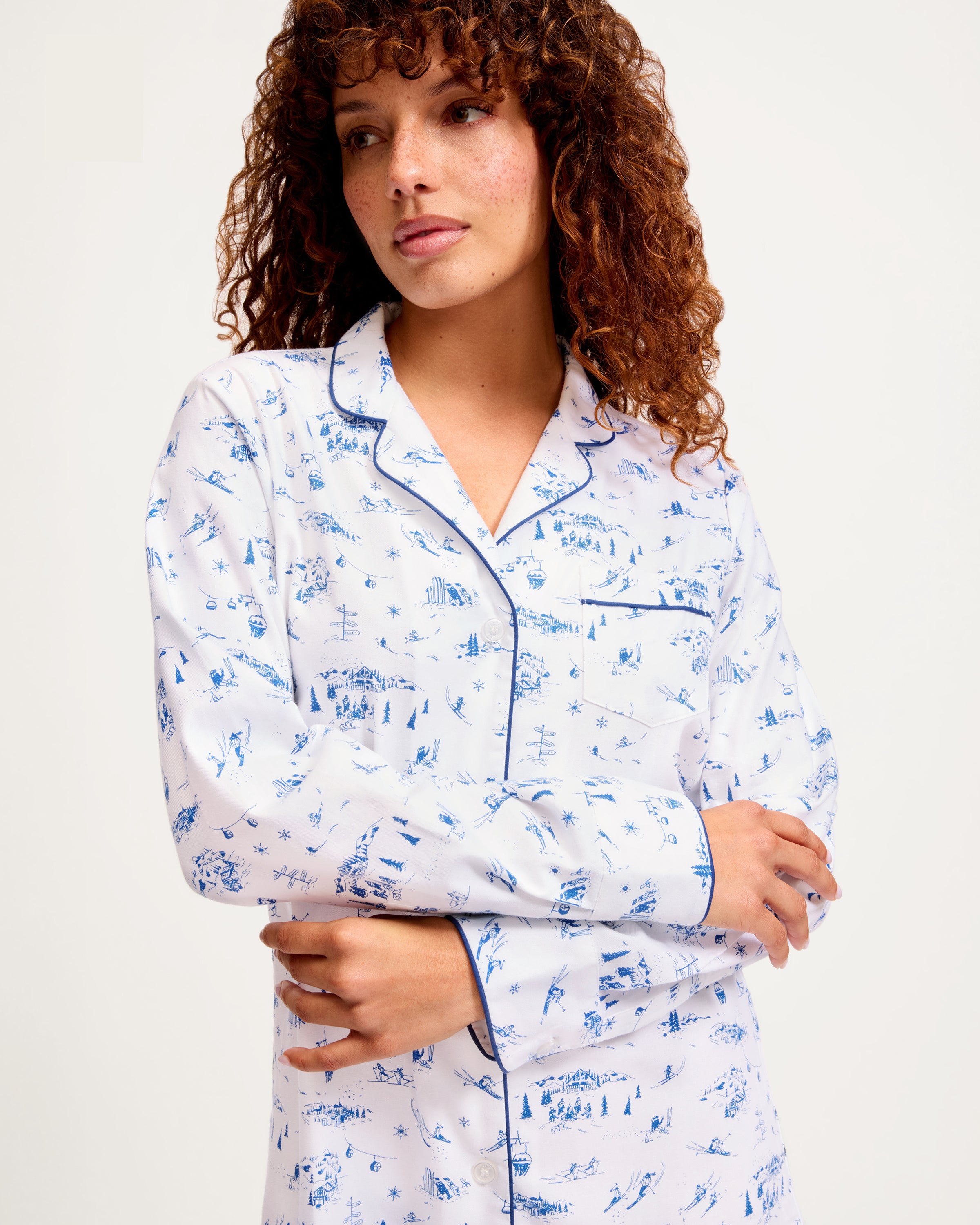 The Women's Twill Nightshirt in Chalet Toile features long sleeves, a white button-up design, a blue scenic print, and dark blue piping on the collar, cuffs, and pocket.