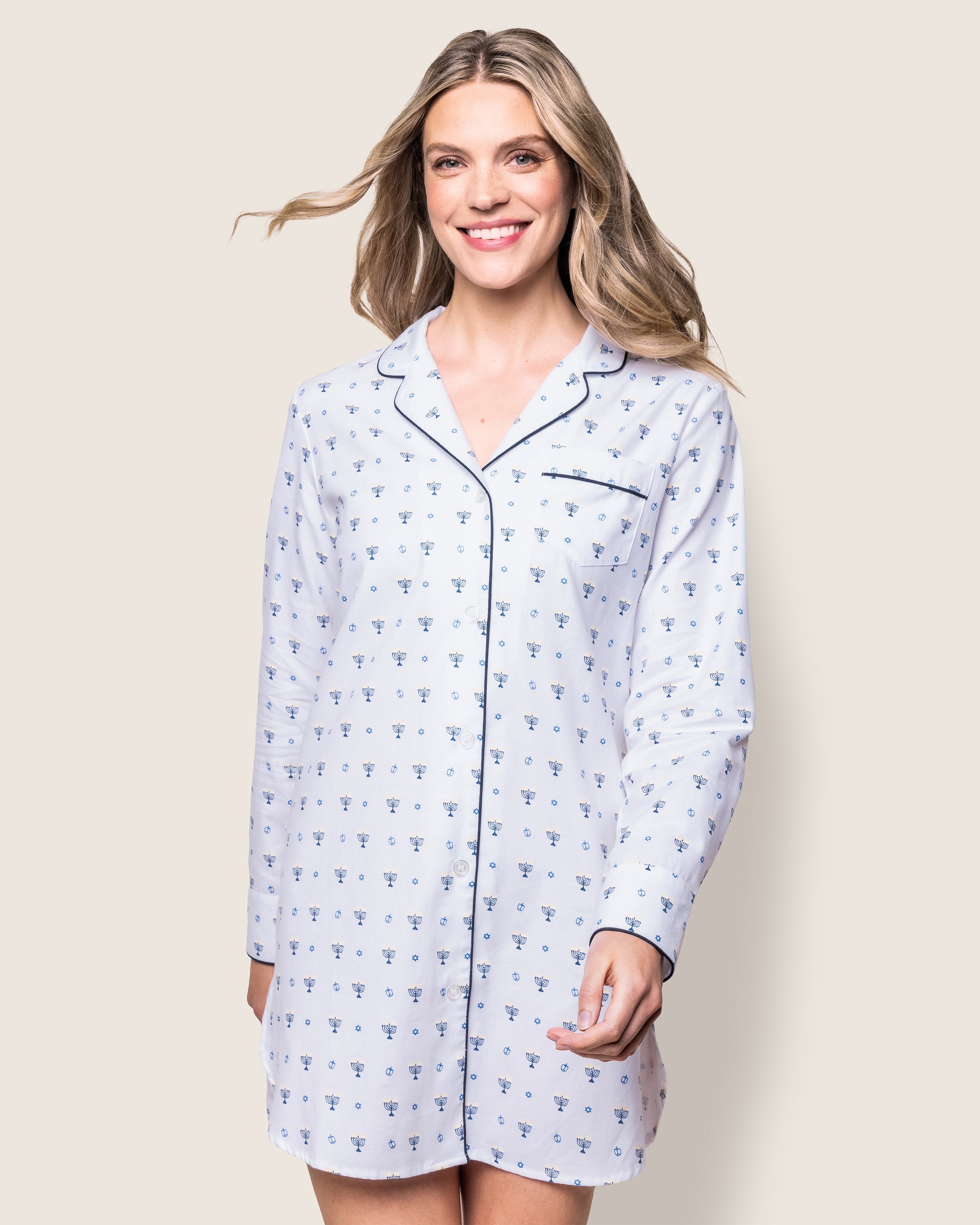 A smiling woman wears the Womens Twill Nightshirt in Happy Hanukkah by Petite Plume, featuring a collared neckline and front pocket. Her long hair flows gracefully as she stands against a plain light background, echoing cozy Hanukkah vibes for the festival of lights.