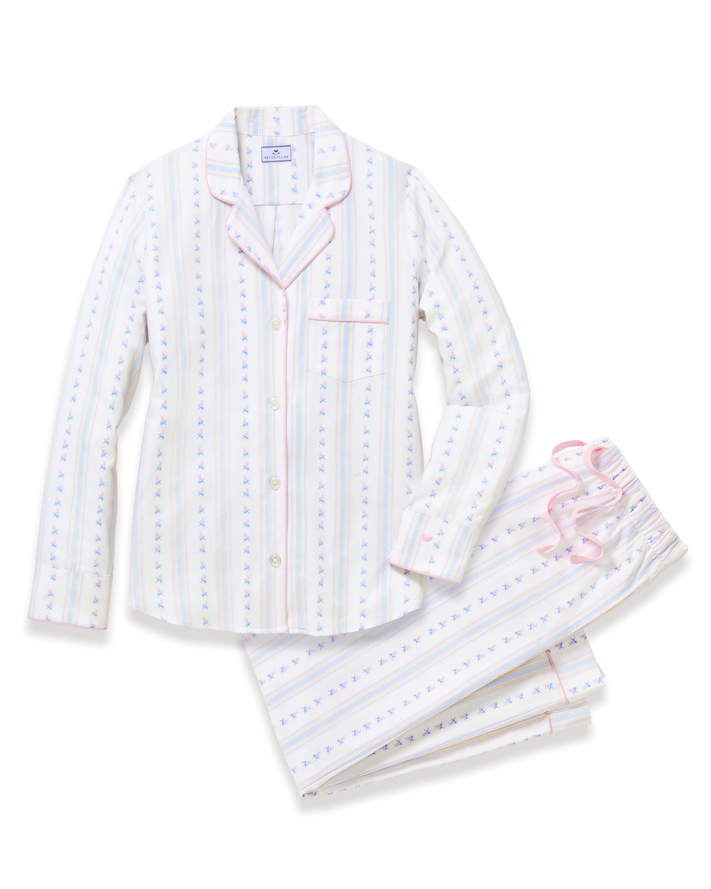 A woman with long curly hair stands barefoot against a plain light background, wearing the Women's Twill Pajama Set in Cottage Stripe—white pajama pants and a matching long-sleeve top with pastel vertical stripes and small dots.