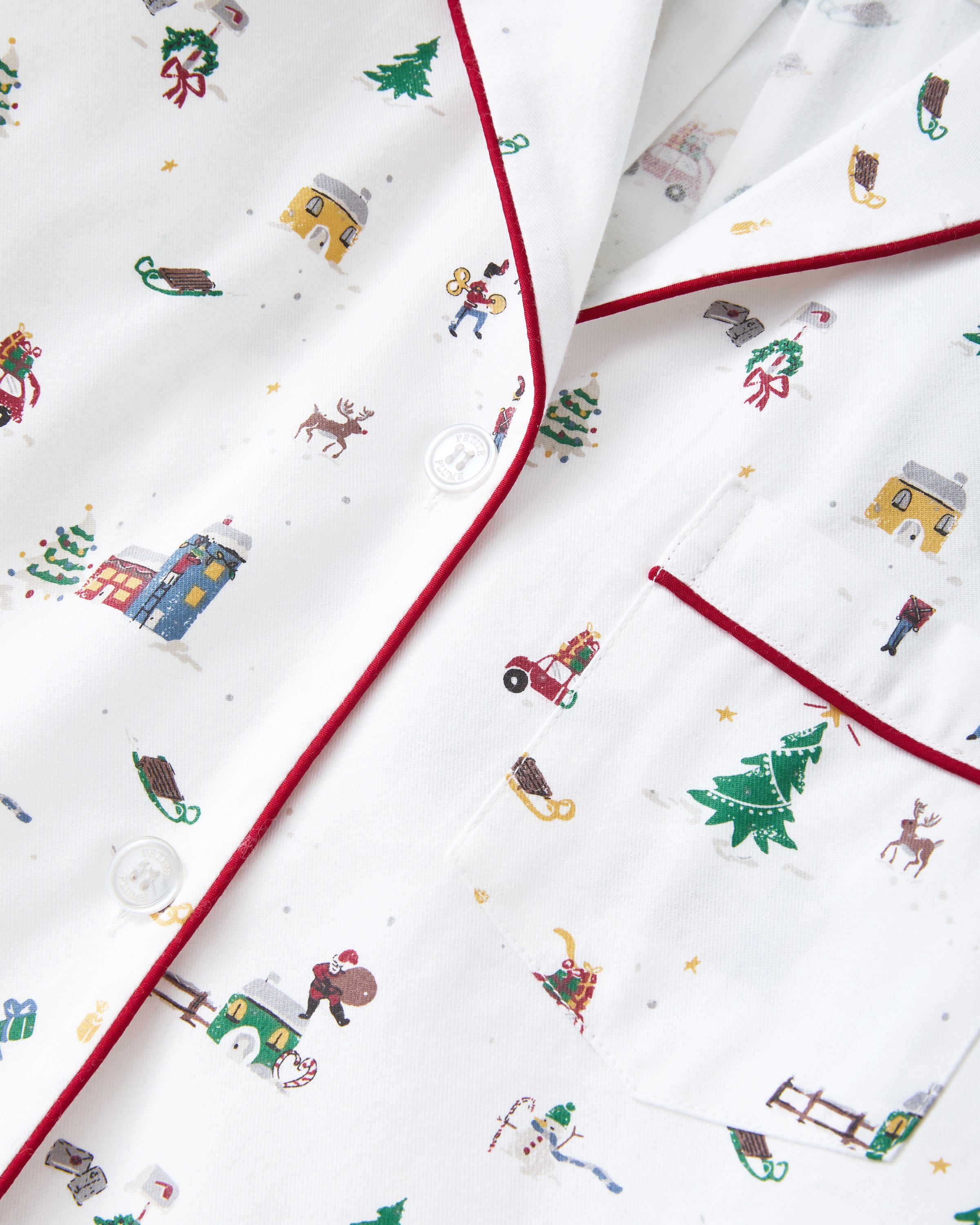 Women's Twill Pajama Set in Holiday Town: white pajama set with red piping, featuring festive prints of Christmas trees, cars, and skiers. Includes a long-sleeve button-up top with a pocket and matching drawstring pants.