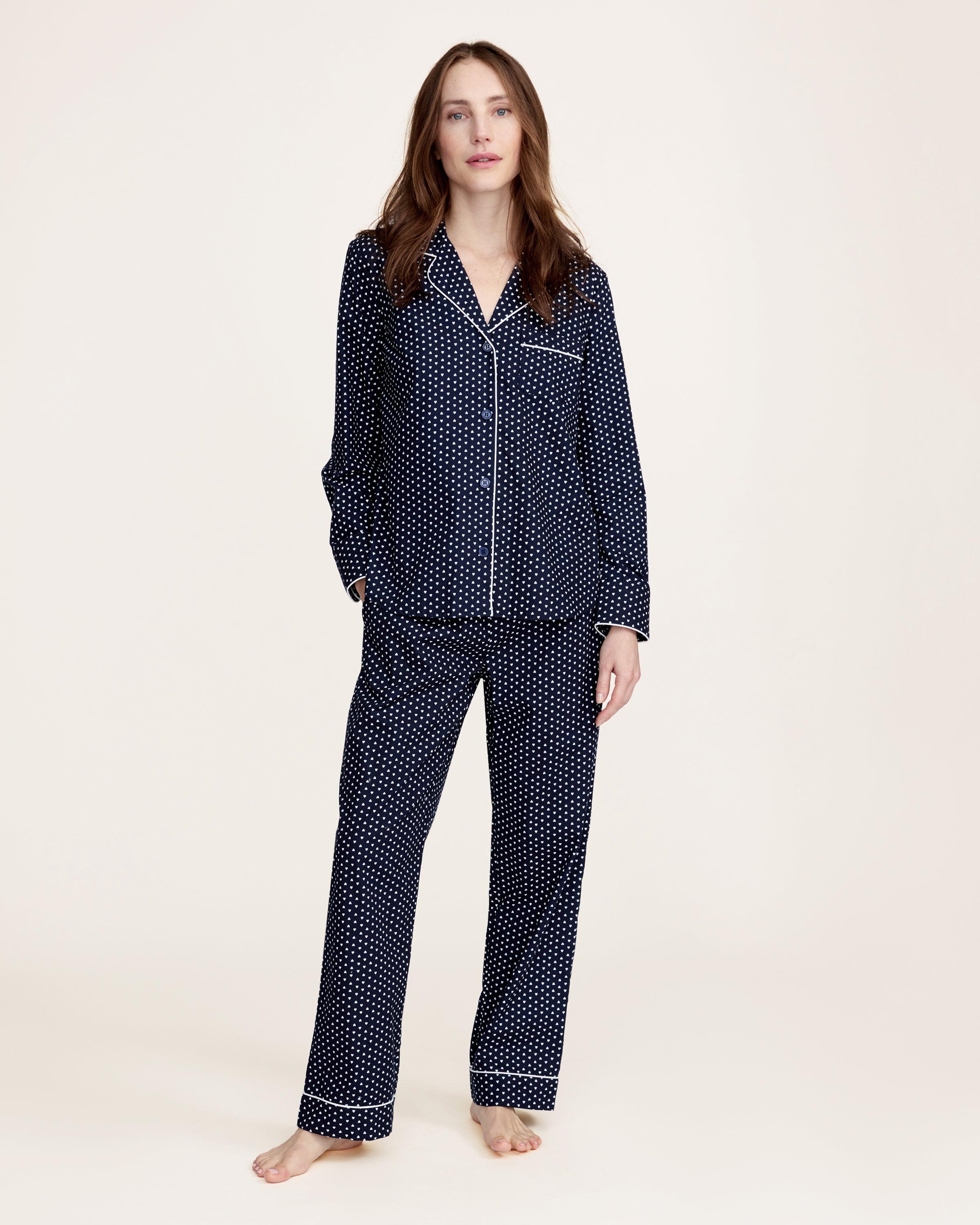 The Women's Twill Pajama Set in Midnight Hearts features a navy blue, long-sleeve top with a collar, button-down front, white heart print, and white piping on the edges and pocket, paired with matching pants.