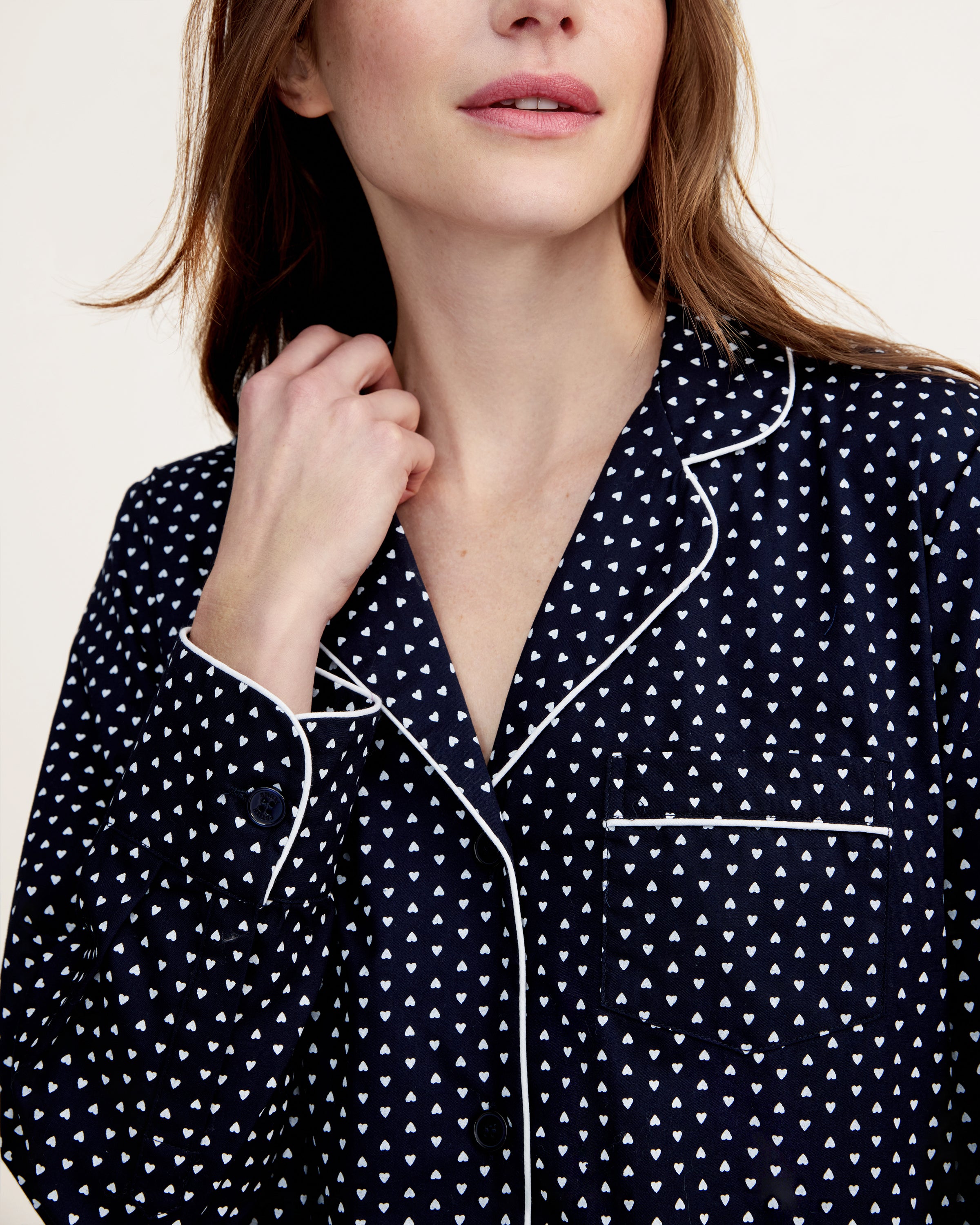 The Women's Twill Pajama Set in Midnight Hearts features a navy blue, long-sleeve top with a collar, button-down front, white heart print, and white piping on the edges and pocket, paired with matching pants.