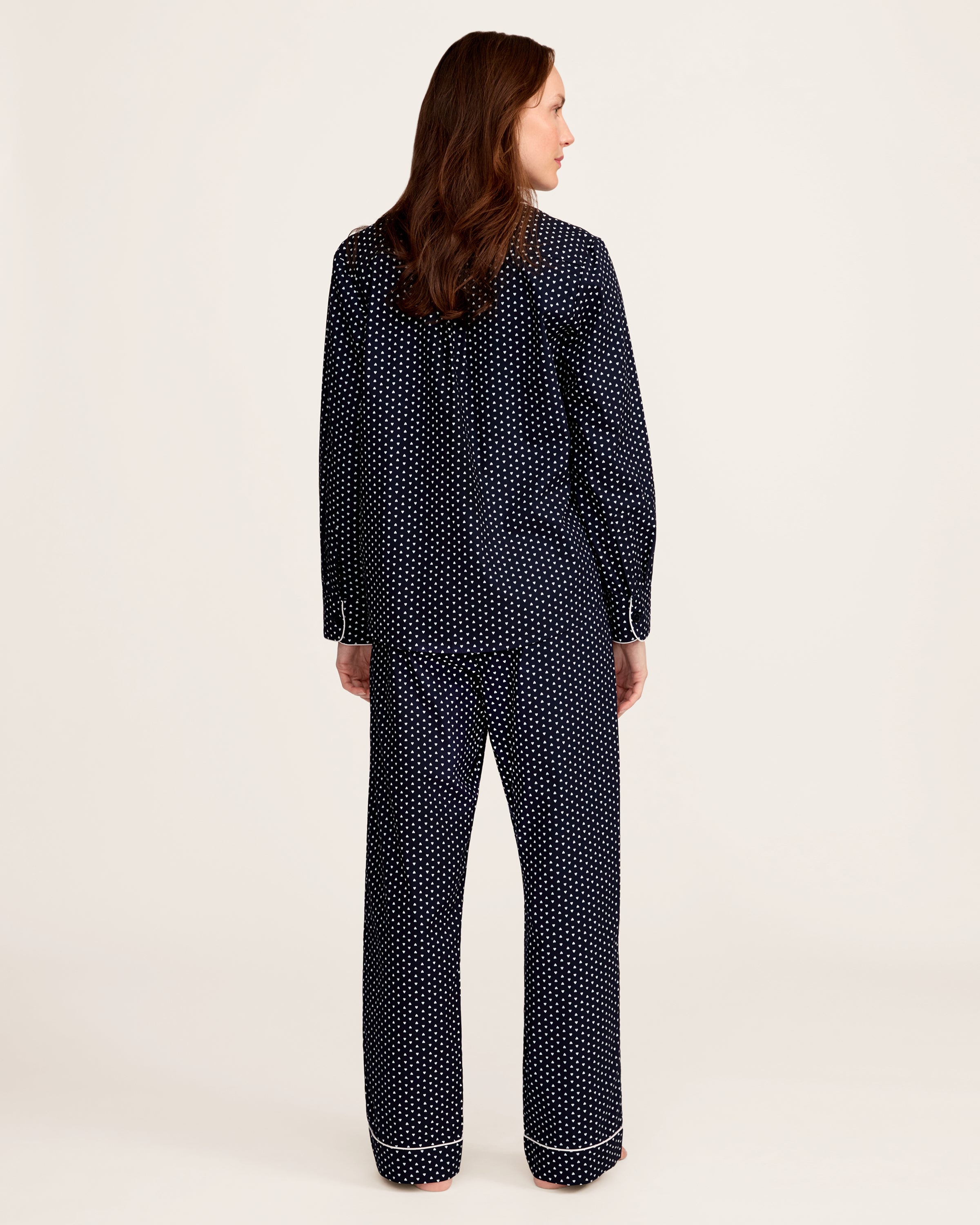 The Women's Twill Pajama Set in Midnight Hearts features a navy blue, long-sleeve top with a collar, button-down front, white heart print, and white piping on the edges and pocket, paired with matching pants.