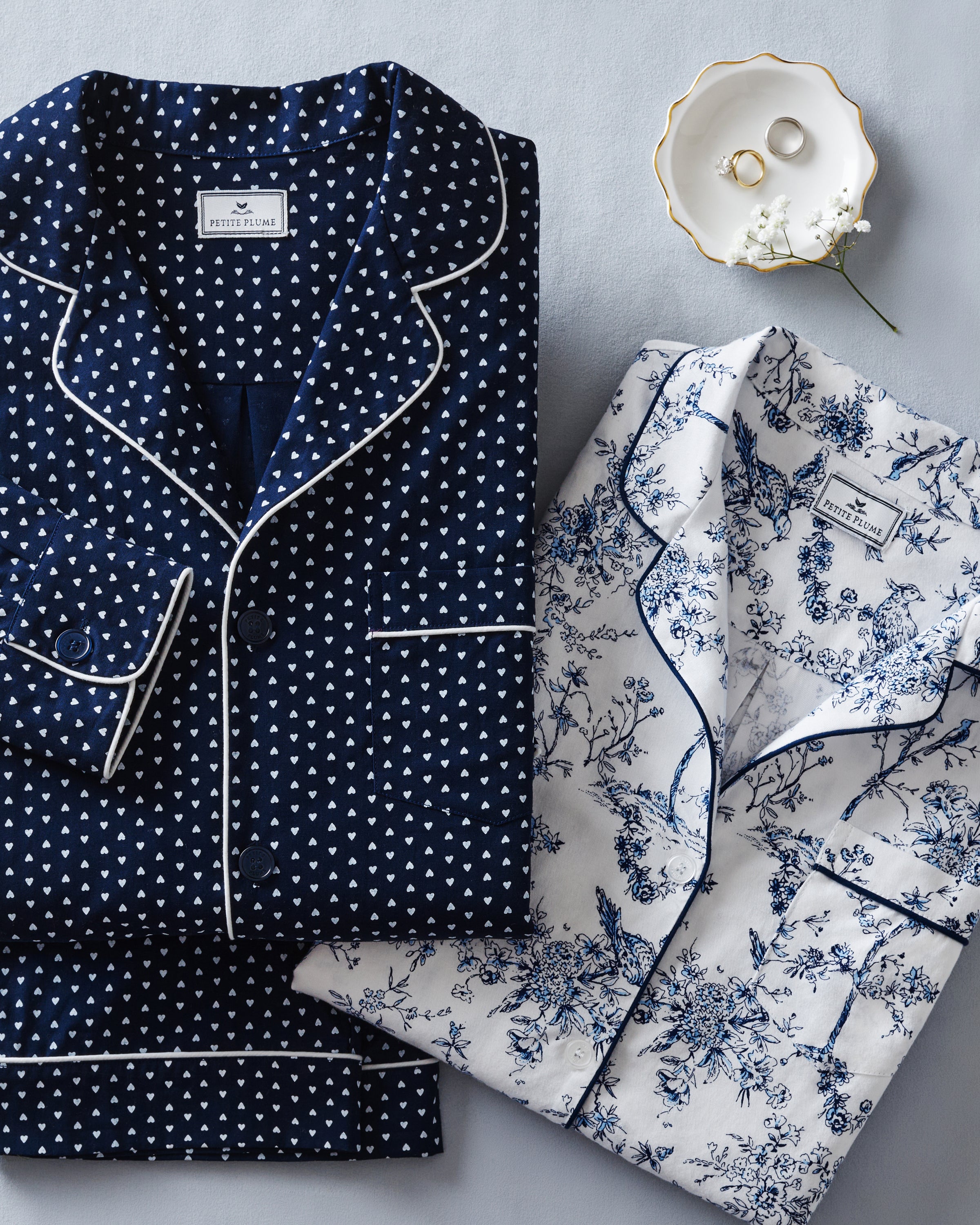 The Women's Twill Pajama Set in Midnight Hearts features a navy blue, long-sleeve top with a collar, button-down front, white heart print, and white piping on the edges and pocket, paired with matching pants.