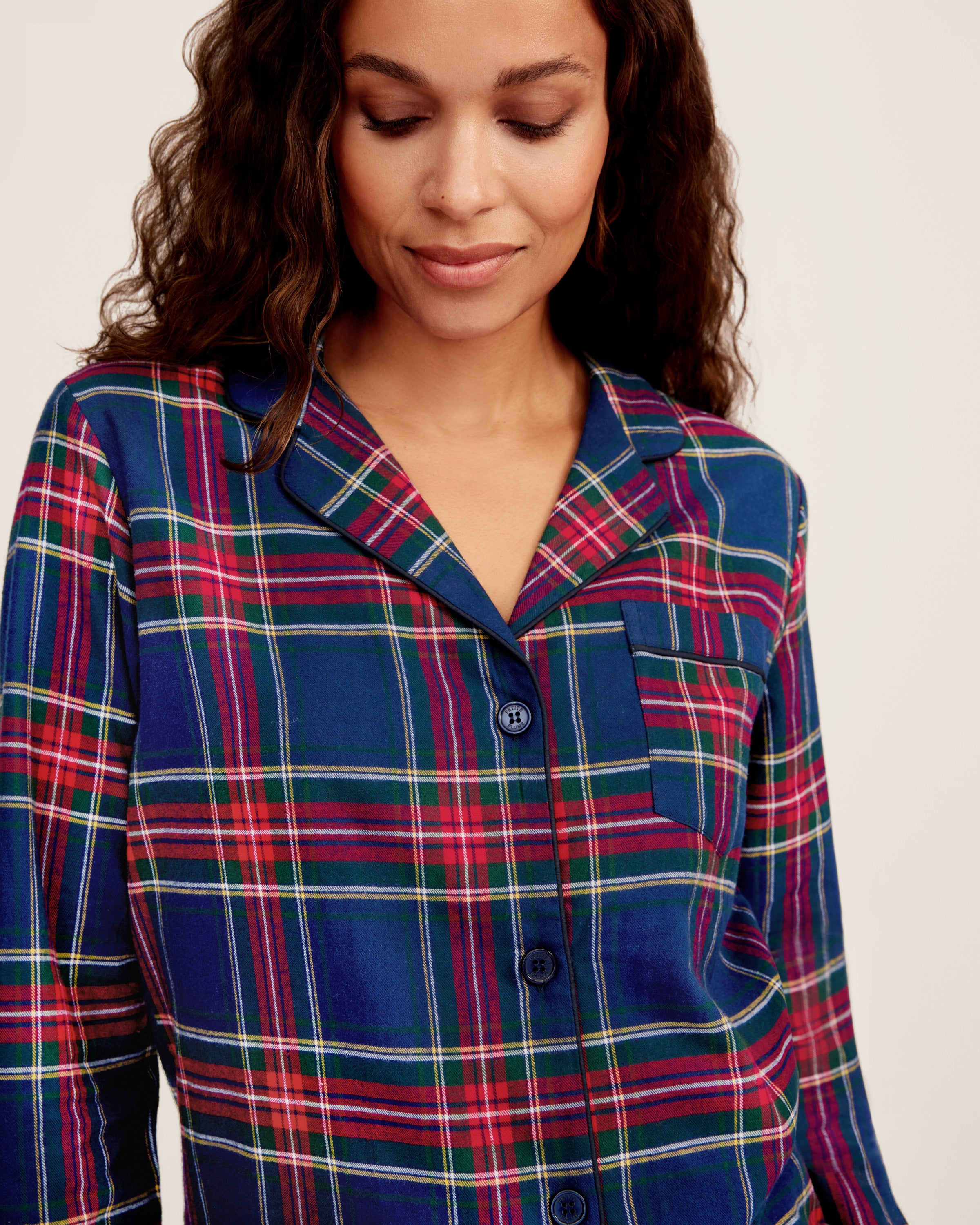 Close-up of Windsor Tartan fabric with red, green, and white stripes on navy by Petite Plume. The soft, brushed cotton texture resembles a classic pajama set with a button and lapel for added coziness.