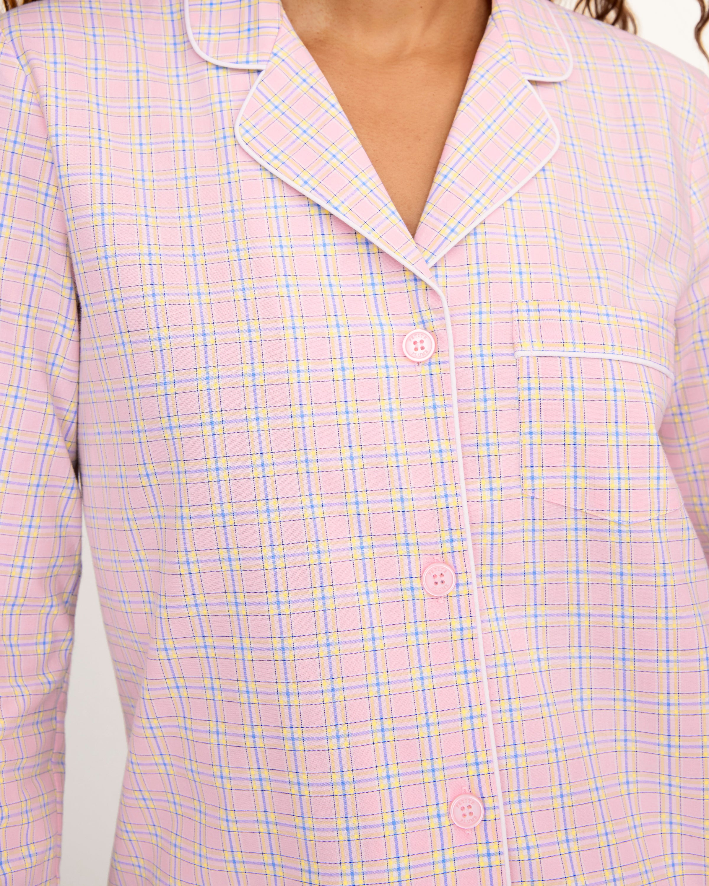 A woman with long curly hair wears the Women's Twill Pajama Set in Peony Plaid, standing barefoot against a plain light background and facing the camera with a relaxed expression.