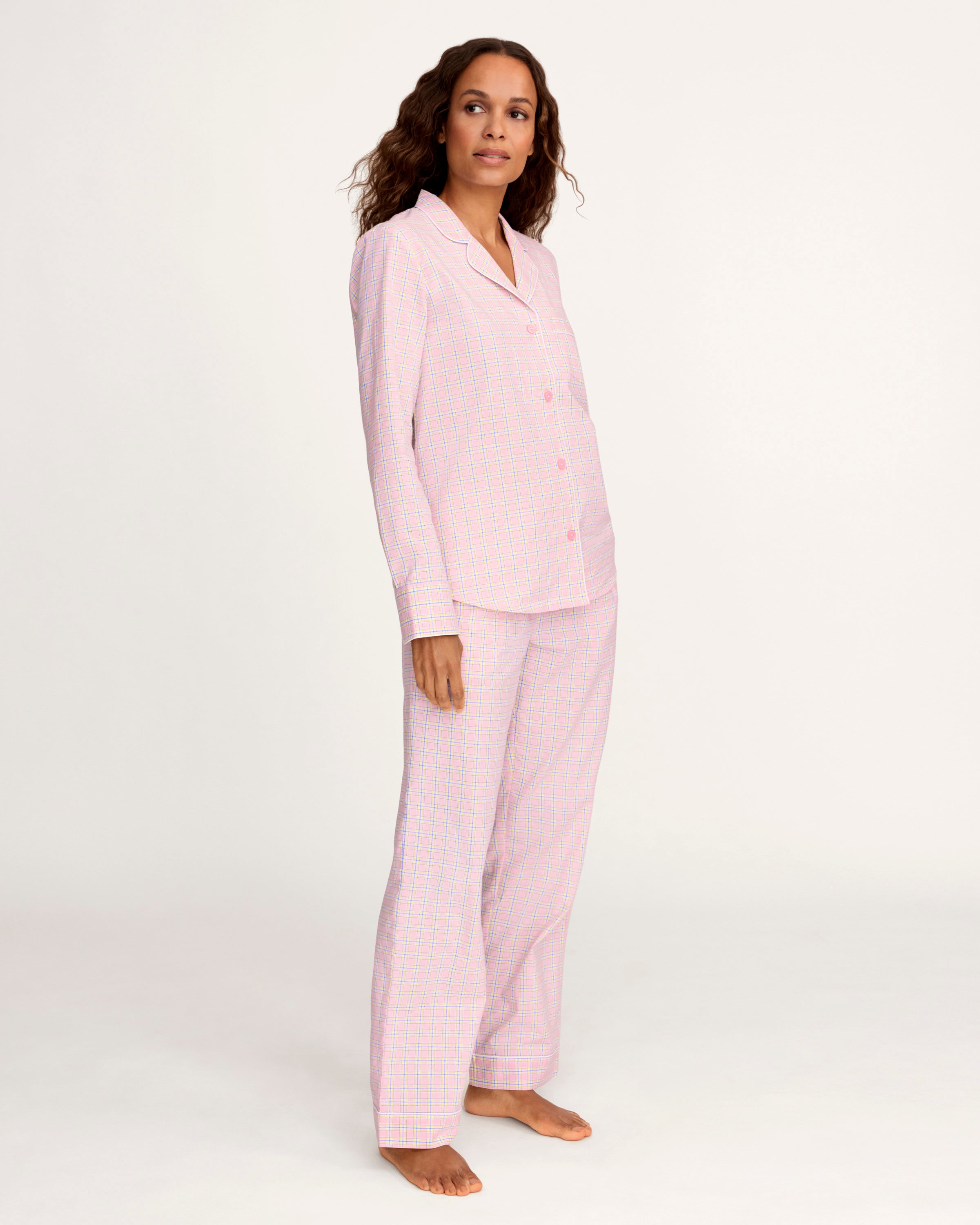 A woman with long curly hair wears the Women's Twill Pajama Set in Peony Plaid, standing barefoot against a plain light background and facing the camera with a relaxed expression.