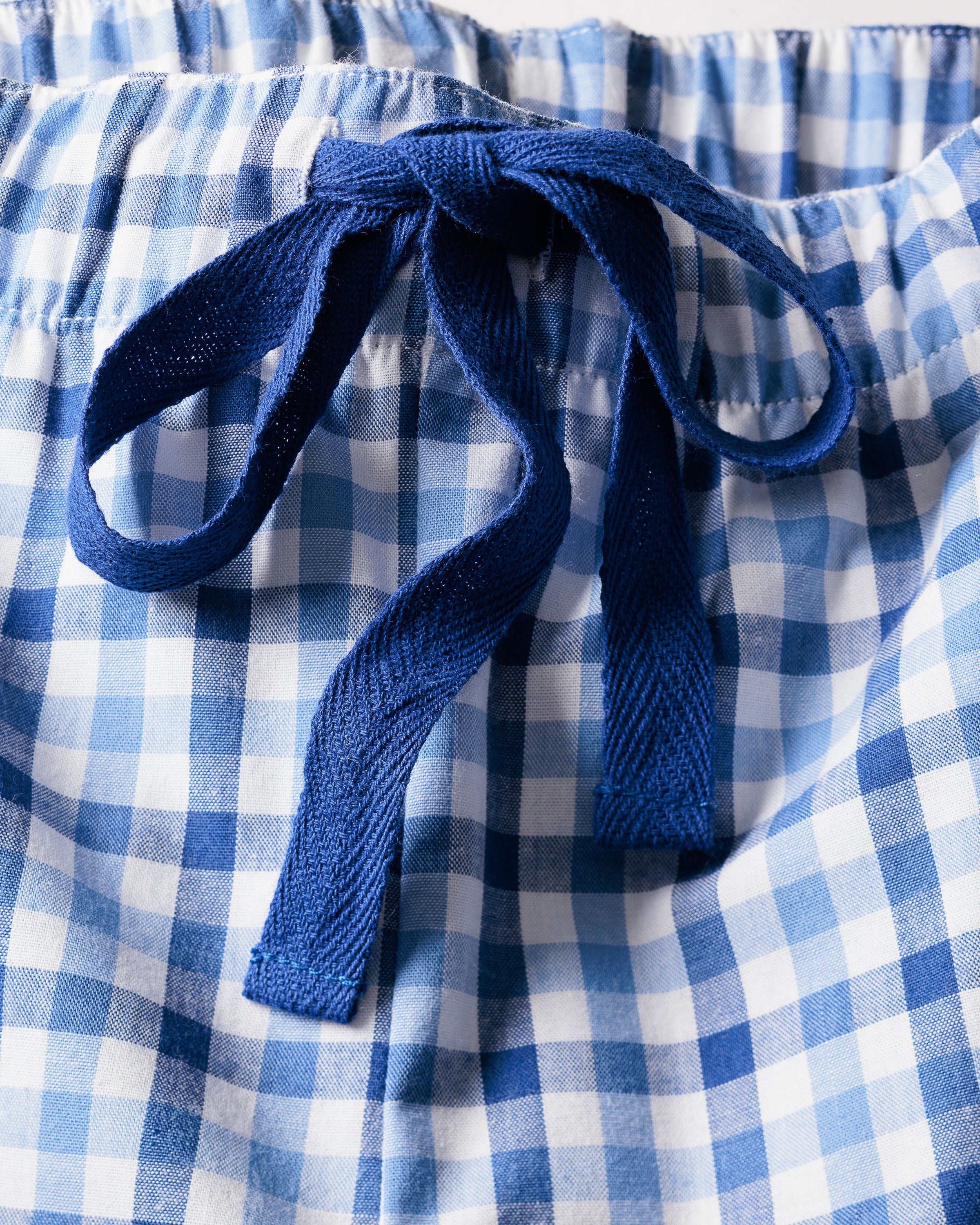 Close-up of Petite Plumes Womens Twill Pajama Set in Royal Blue Gingham. It features an elastic waistband with a charming blue ribbon bow and a checkered pattern of varying blue shades, crafted from 100% cotton.