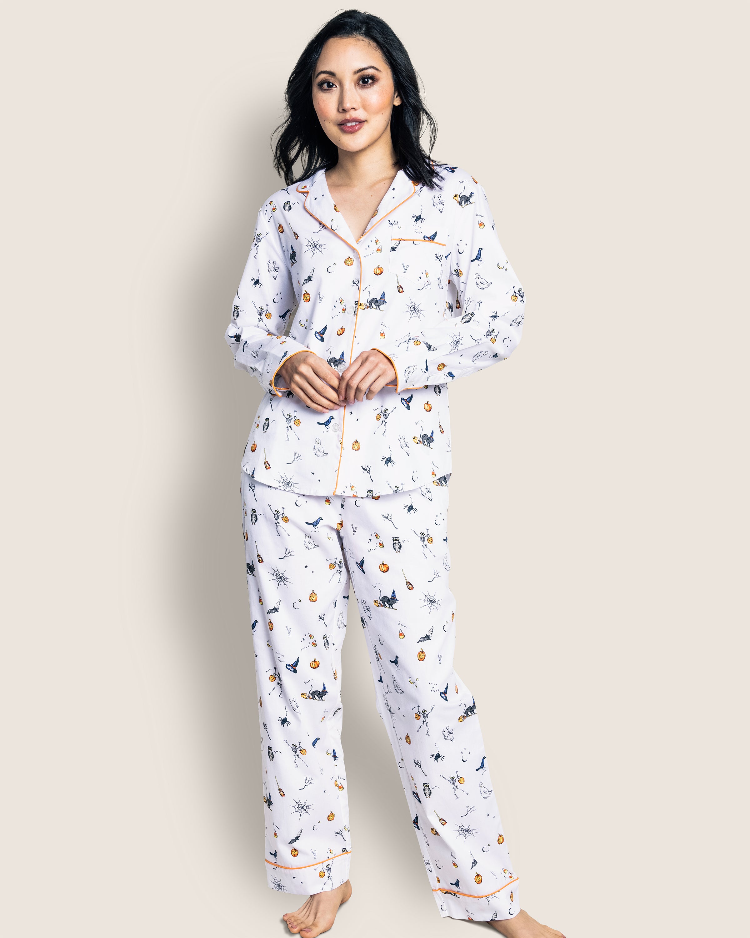 A barefoot person models the Womens Twill Pajama Set in Trick or Treat by Petite Plume, featuring white cotton twill with festive orange piping.