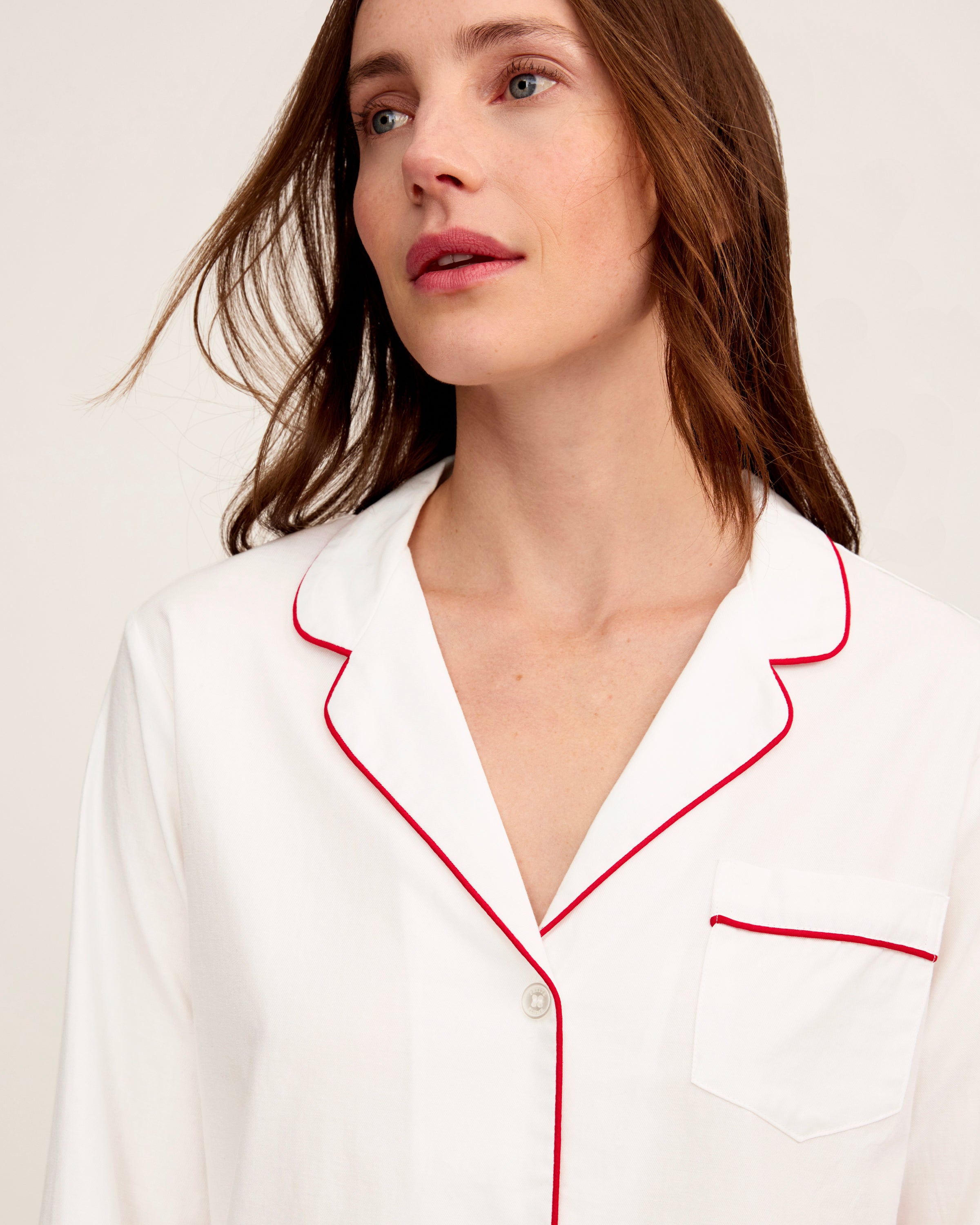 A woman stands barefoot in the Women's Twill Pajama Set in White with Red Piping against a plain, light background.