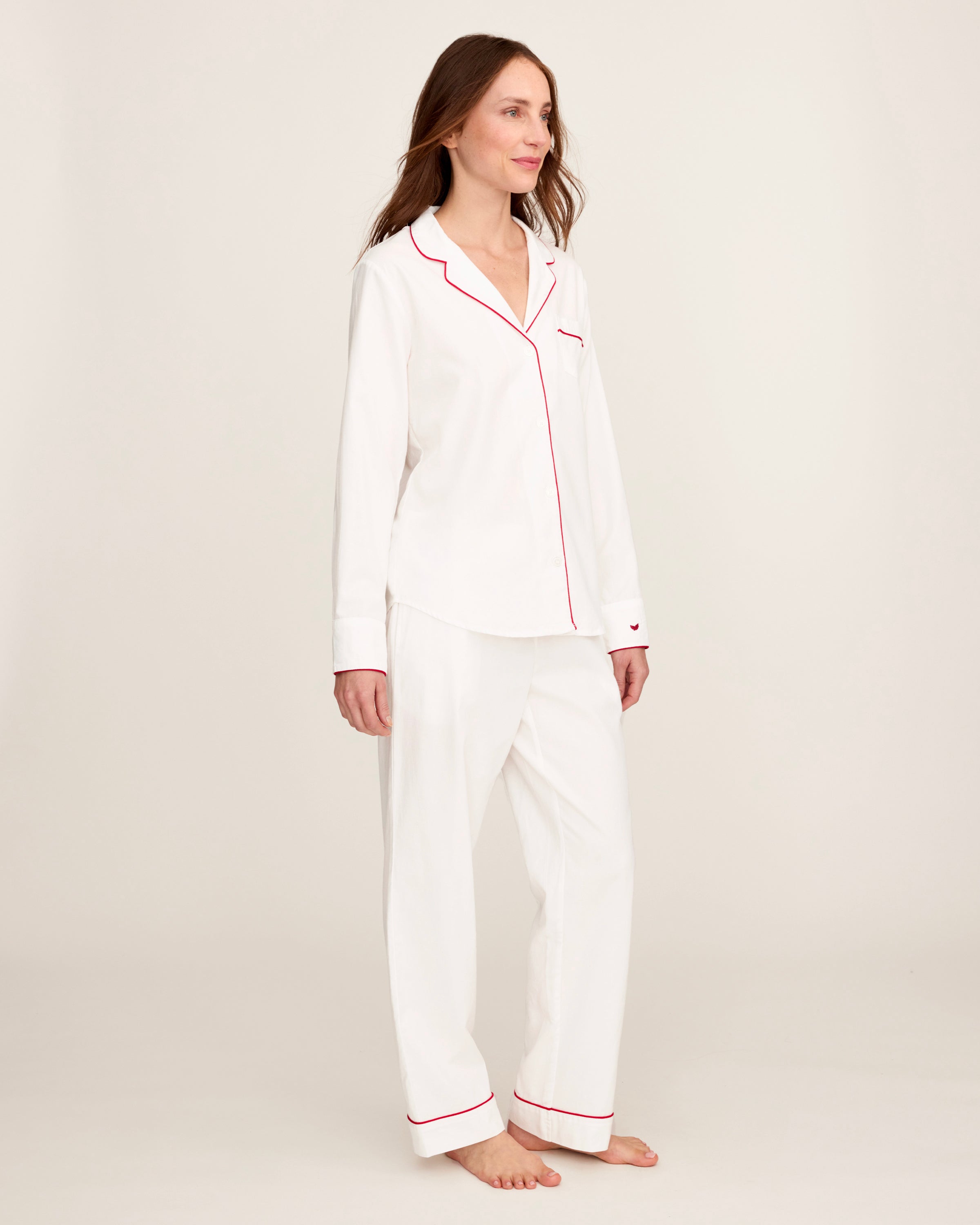 A woman stands barefoot in the Women's Twill Pajama Set in White with Red Piping against a plain, light background.