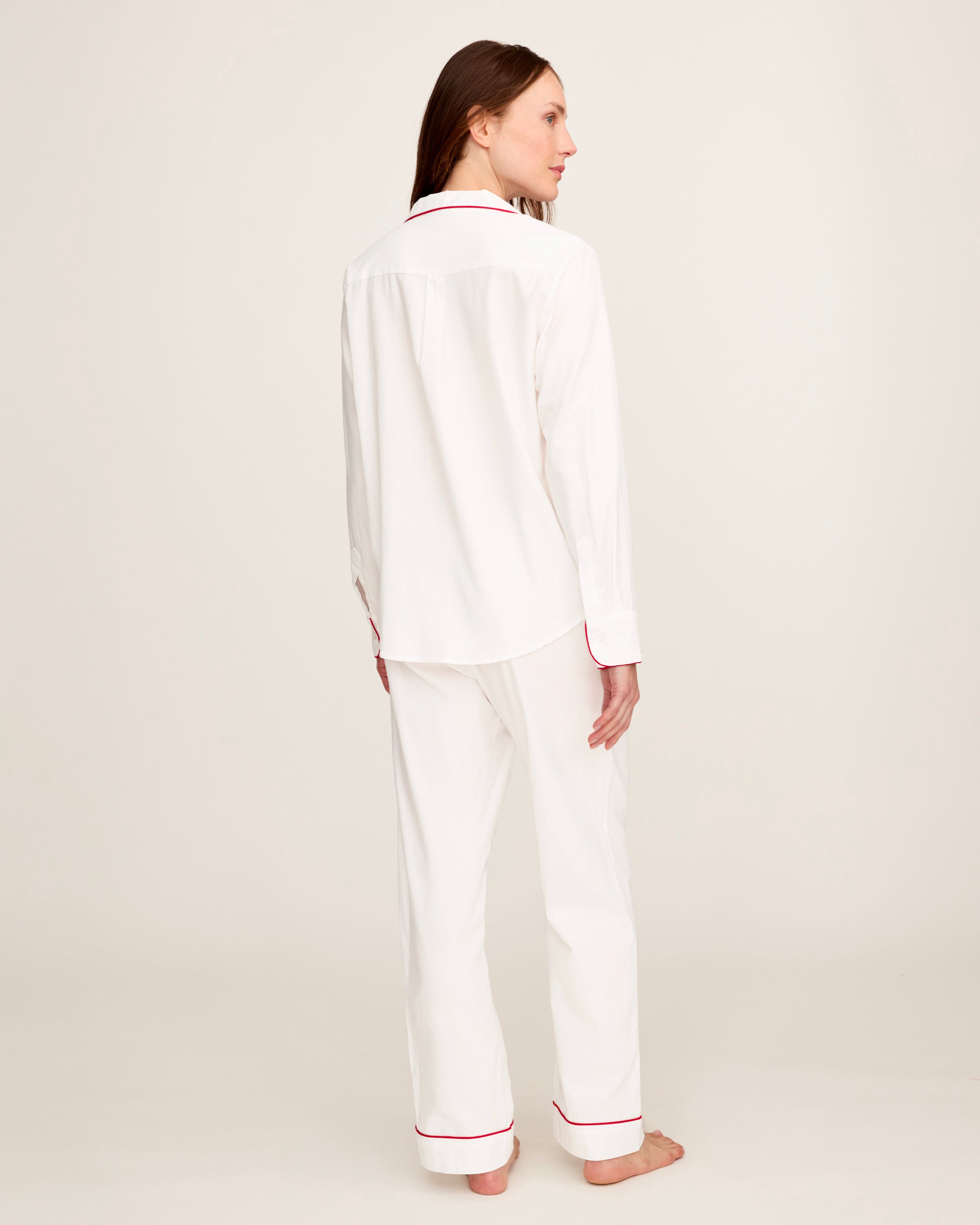 A woman stands barefoot in the Women's Twill Pajama Set in White with Red Piping against a plain, light background.