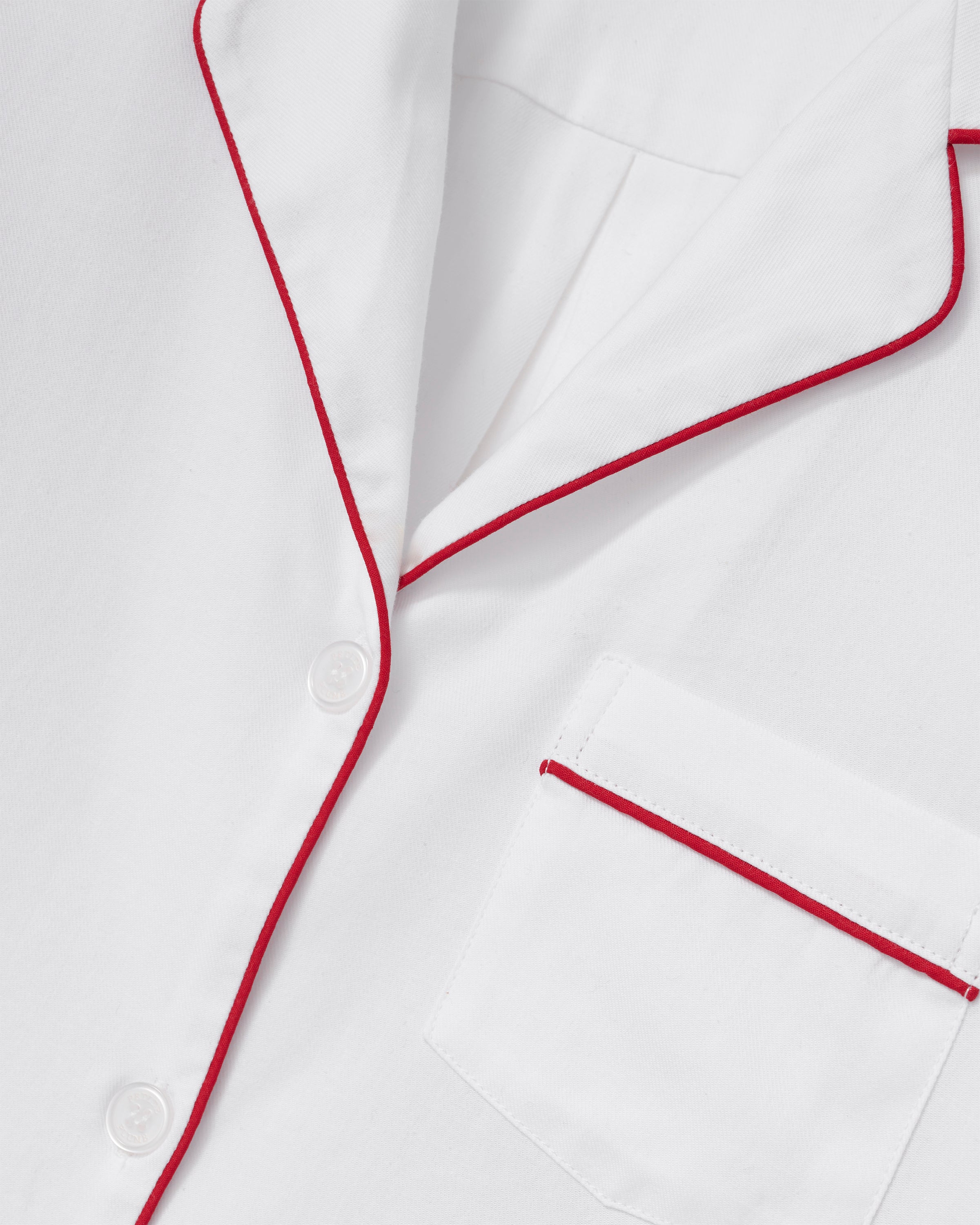 A woman stands barefoot in the Women's Twill Pajama Set in White with Red Piping against a plain, light background.