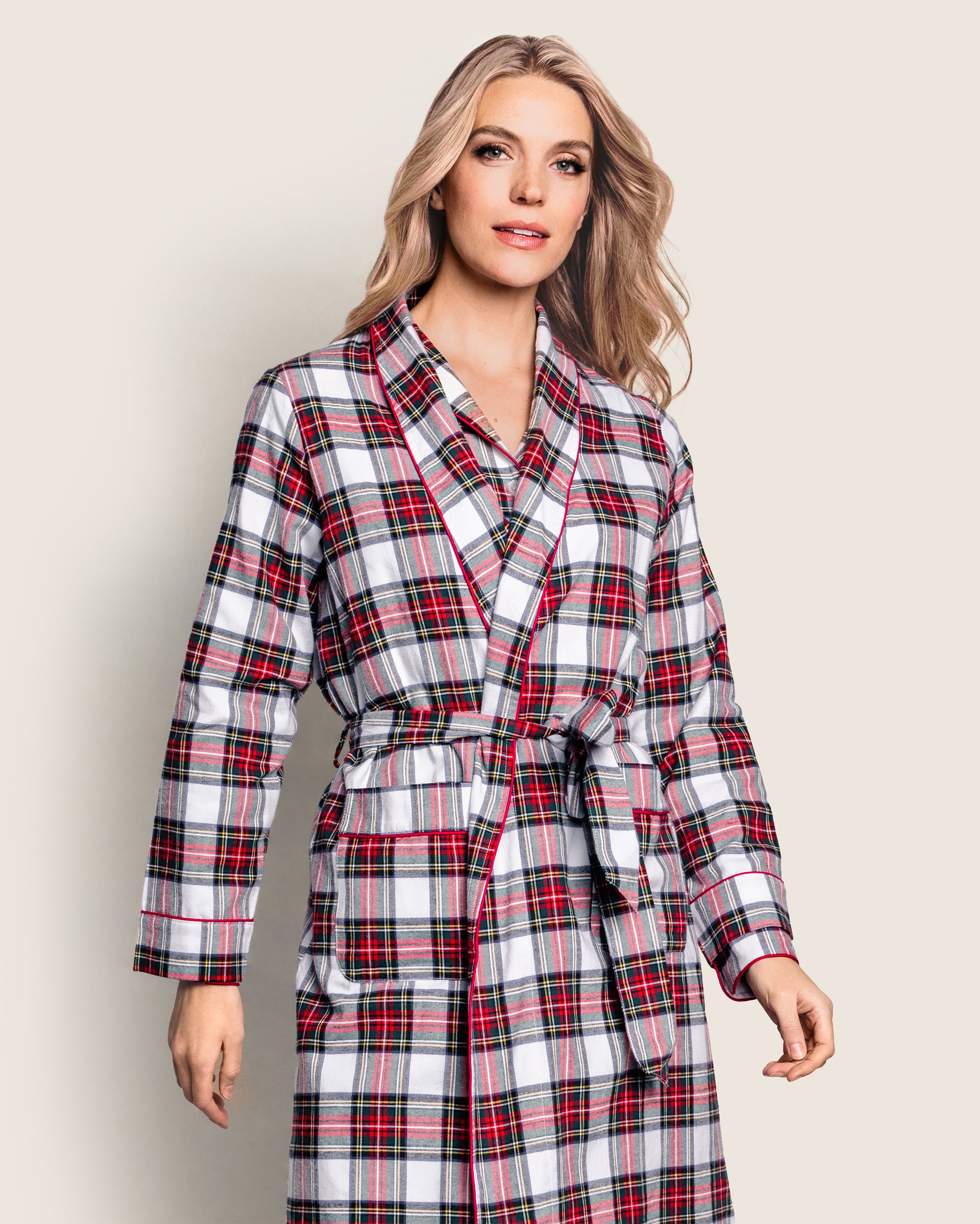 A person smiles against a plain background wearing Petite Plumes Womens Brushed Cotton Robe in red, white, and green Balmoral Tartan. The luxury robe features brushed twill fabric and is elegantly tied at the waist with a belt.