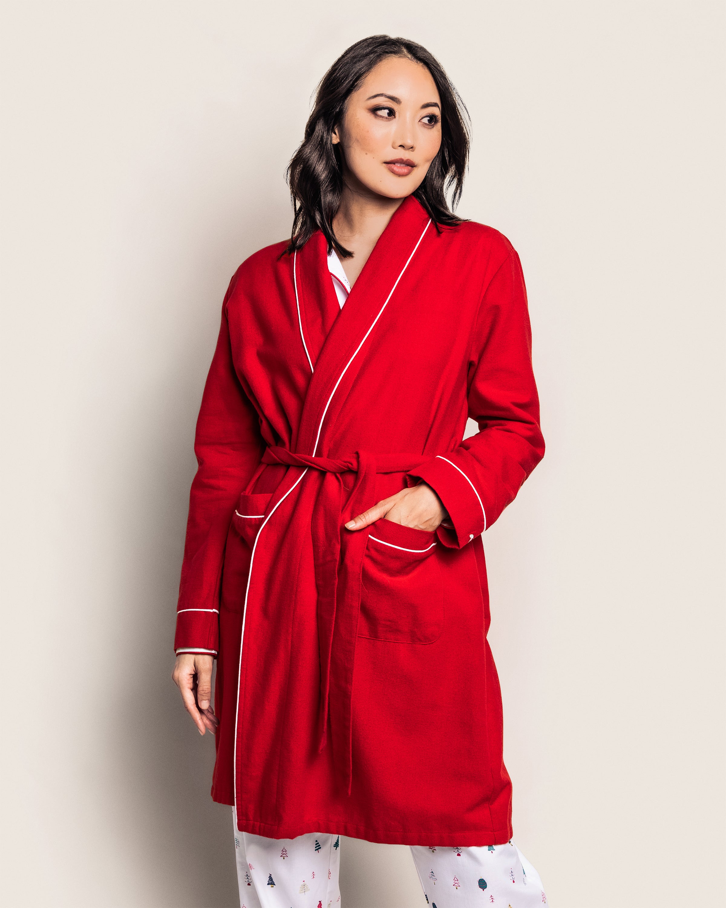 A model showcases Petite Plumes Womens Flannel Robe in Red with White Piping, paired with monogrammed flannel pants. They stand against a plain background, gazing to the side, one hand in their pocket.