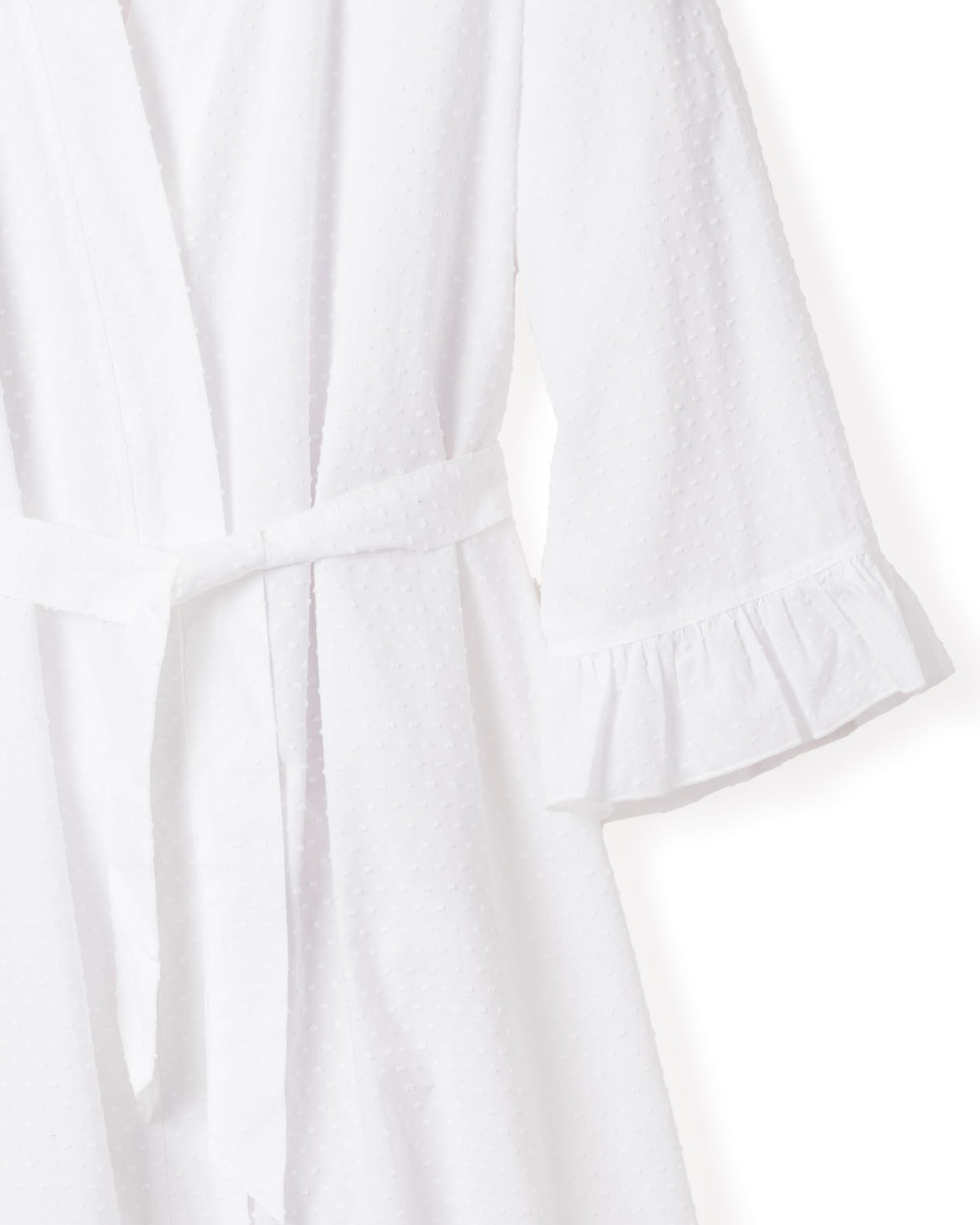 The Womens Swiss Dots Robe in White by Petite Plume features a textured cotton fabric with long sleeves, ruffled cuffs, and a belt. The image highlights its soft texture and elegant design.