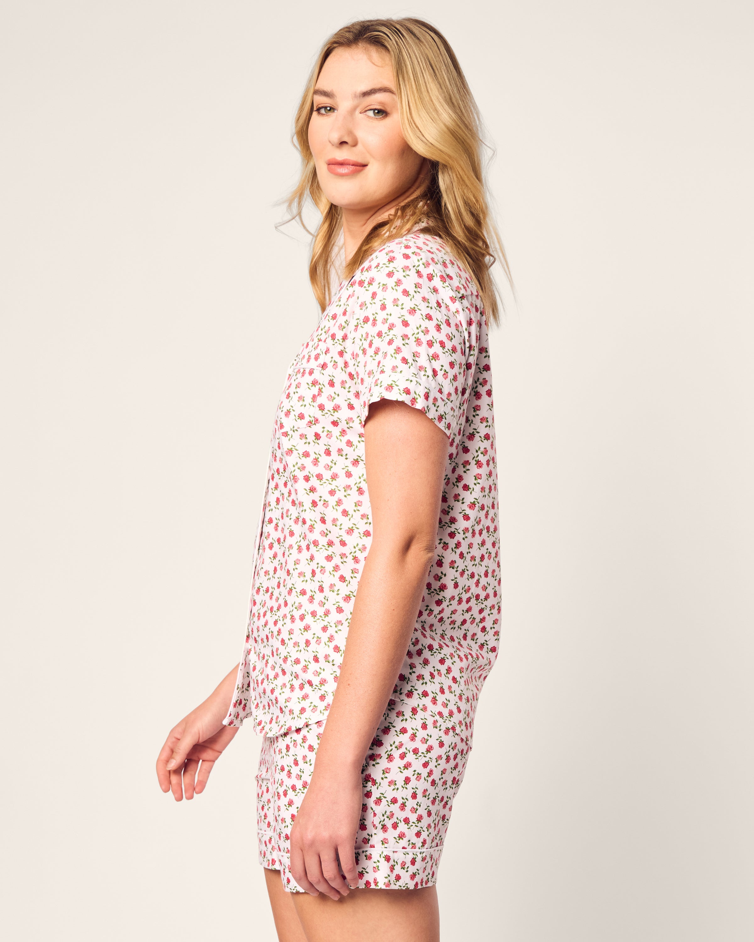 A woman with long blonde hair is wearing the Womens Twill Short Sleeve Short Set in Petite Petals by Petite Plume. She stands sideways, smiling against a plain light background, effortlessly combining comfort and style.