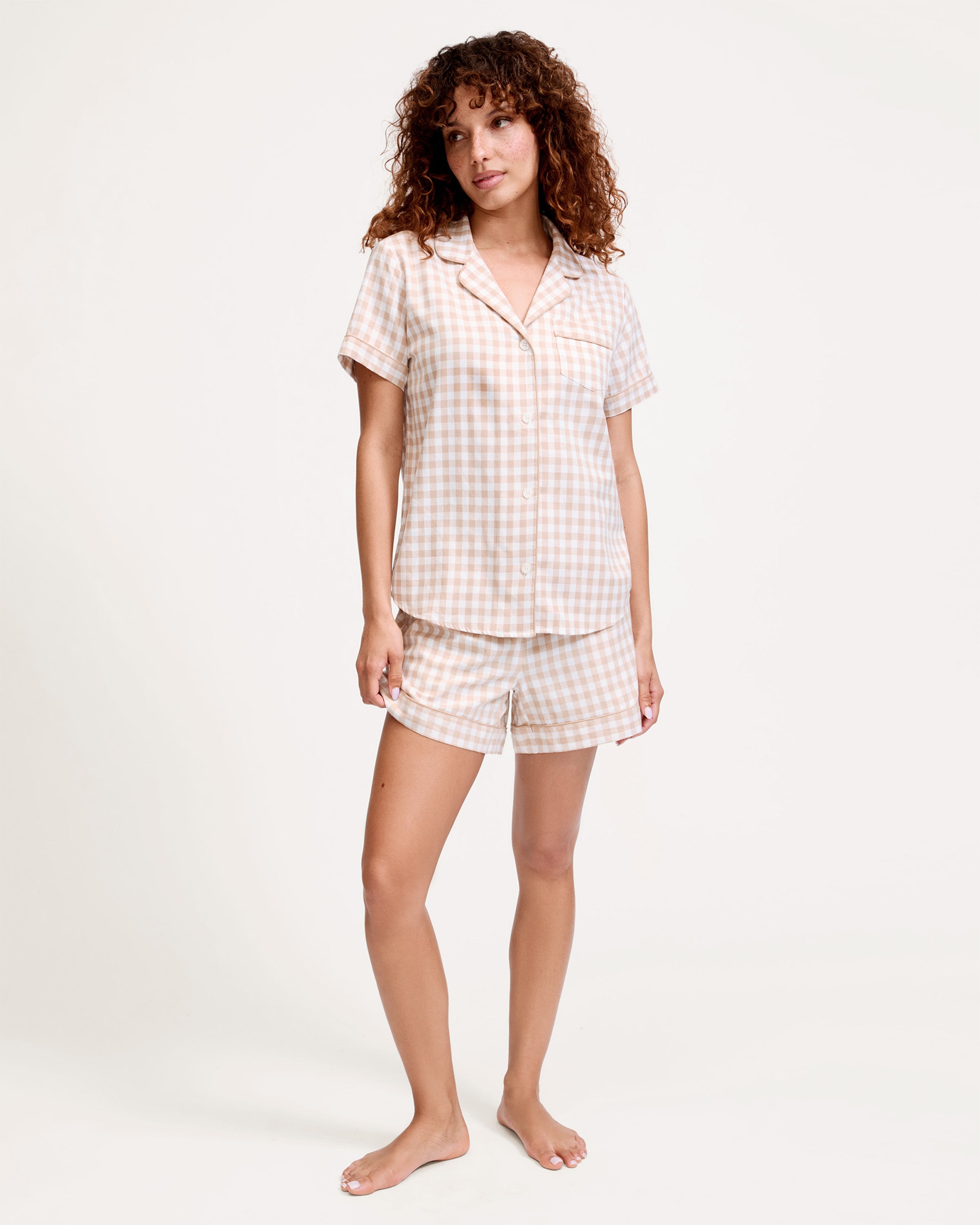 The Women's Twill Short Sleeve Short Set in Camel Gingham features a button-up shirt and matching drawstring shorts with a beige and white gingham pattern.