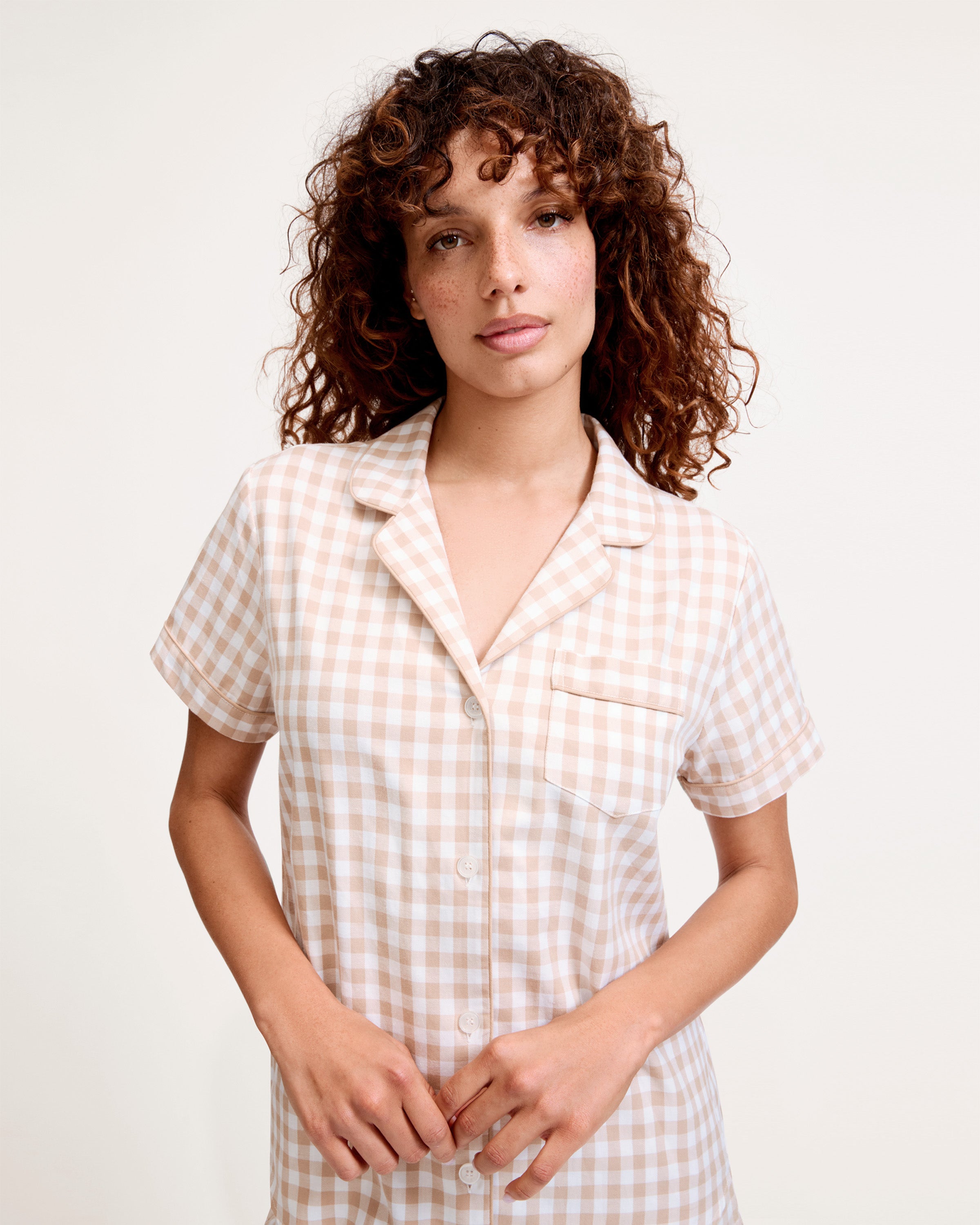 The Women's Twill Short Sleeve Short Set in Camel Gingham features a button-up shirt and matching drawstring shorts with a beige and white gingham pattern.