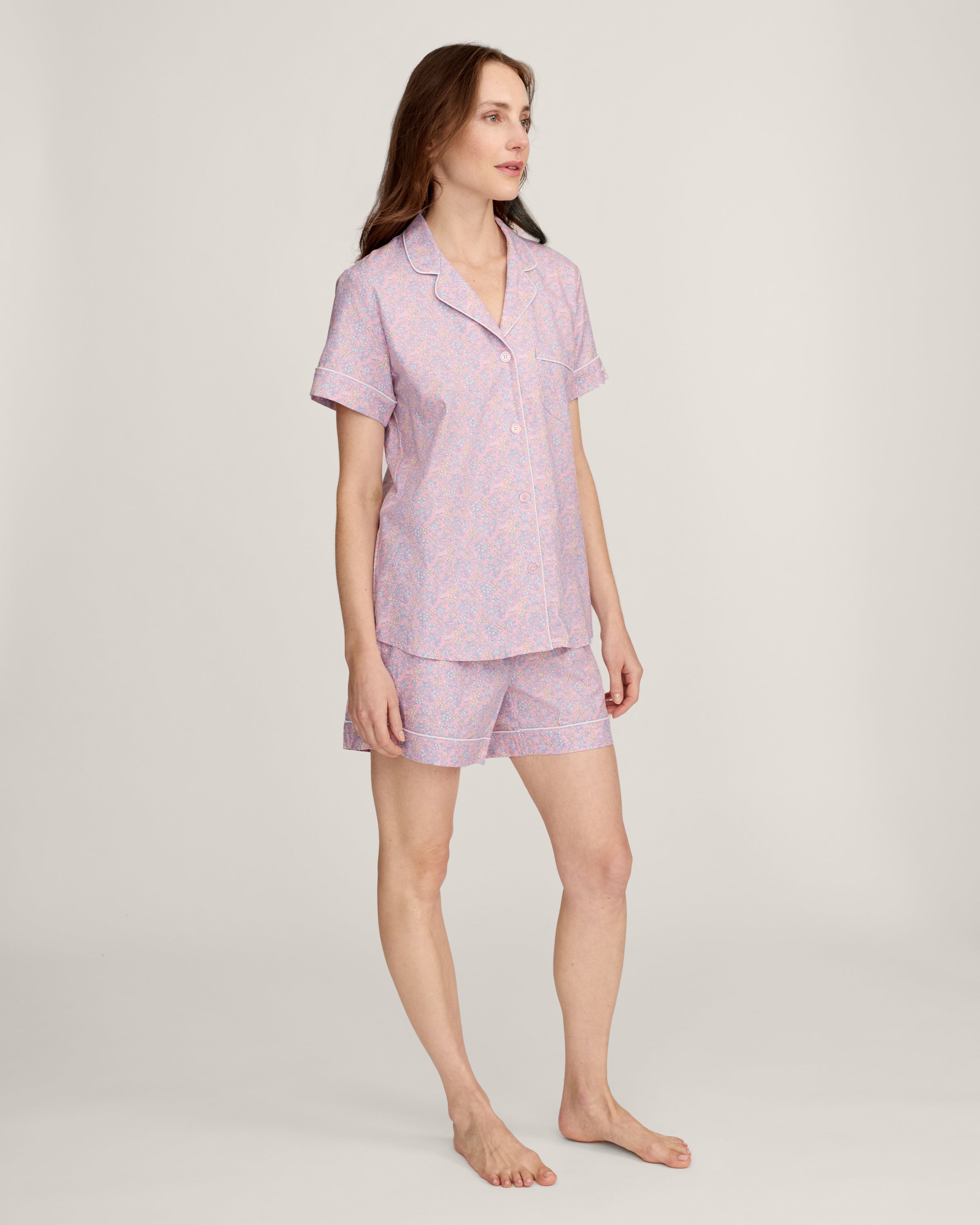 A woman with long brown hair is wearing the Women's Twill Short Sleeve Short Set in Fleur Blush and smiling softly, standing in front of a plain light background.