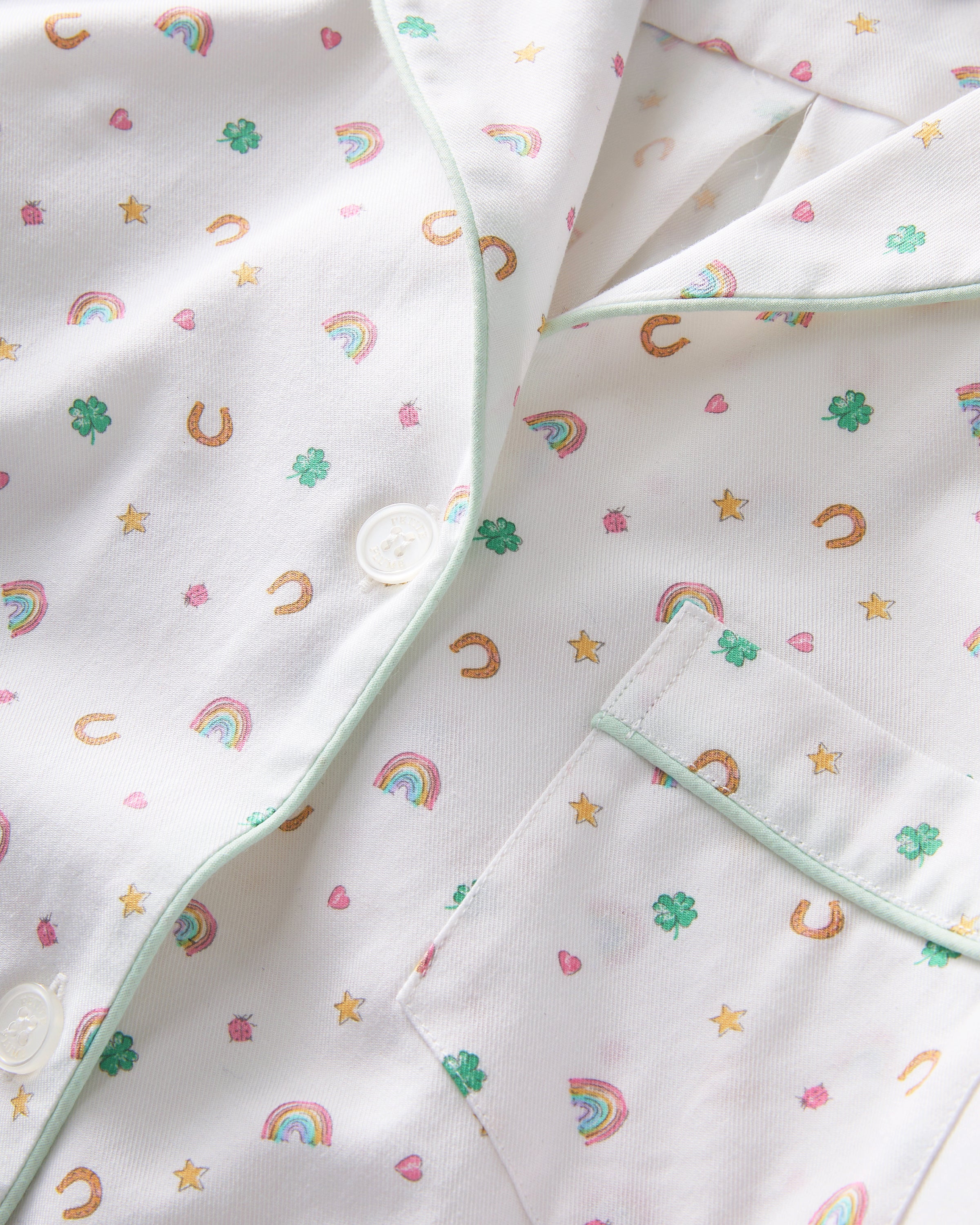 A woman with long, wavy blonde hair wears the Women's Twill Short Sleeve Short Set in Good Luck Charms, featuring a multicolored pattern, standing against a plain light background.