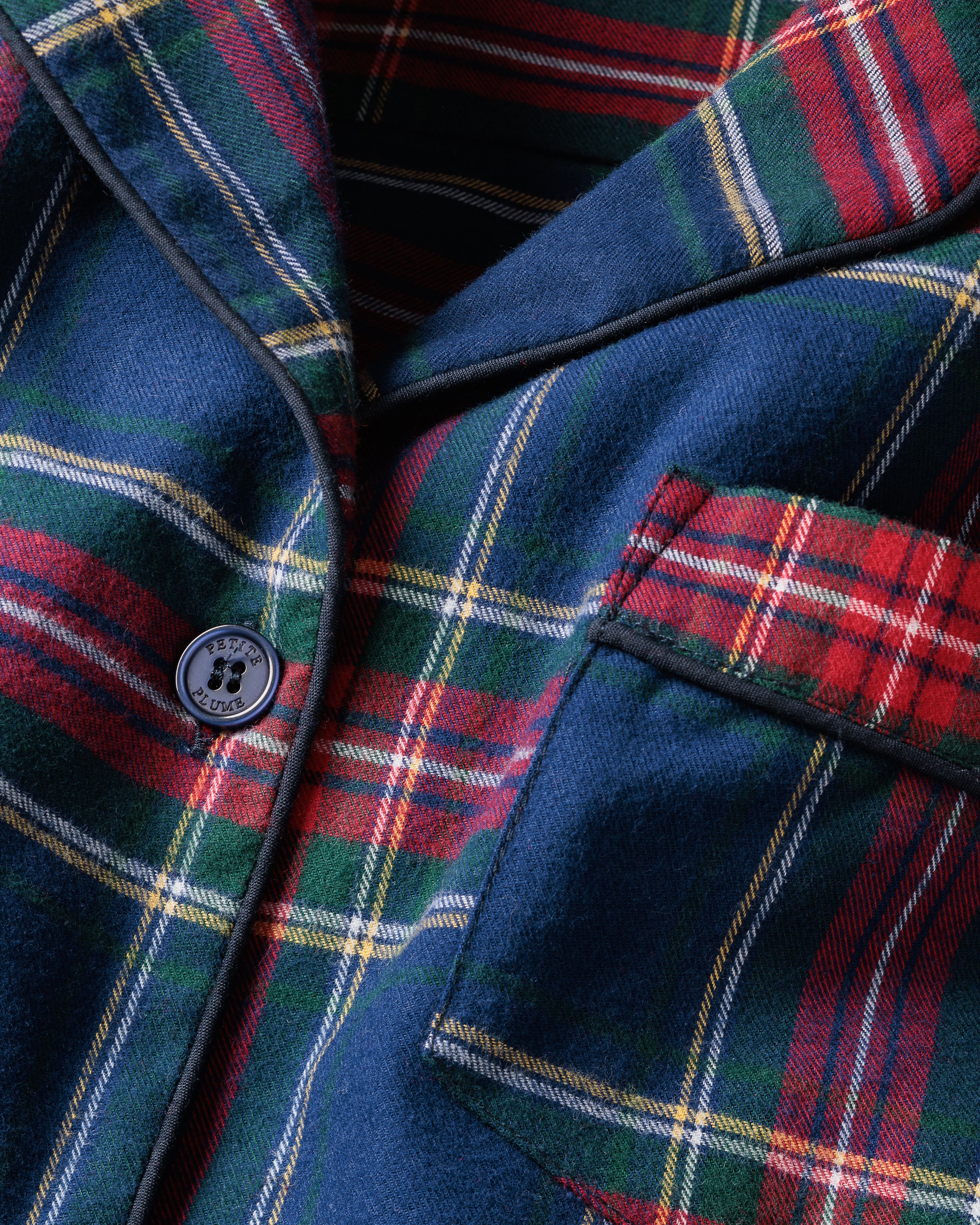 A close-up of Petite Plumes Womens Brushed Cotton Short Sleeve Short Set in Windsor Tartan showcases a blue, red, and green plaid fabric with a button emblem and contrasting piping on the pocket, epitomizing the elegance of luxury cotton sleepwear.