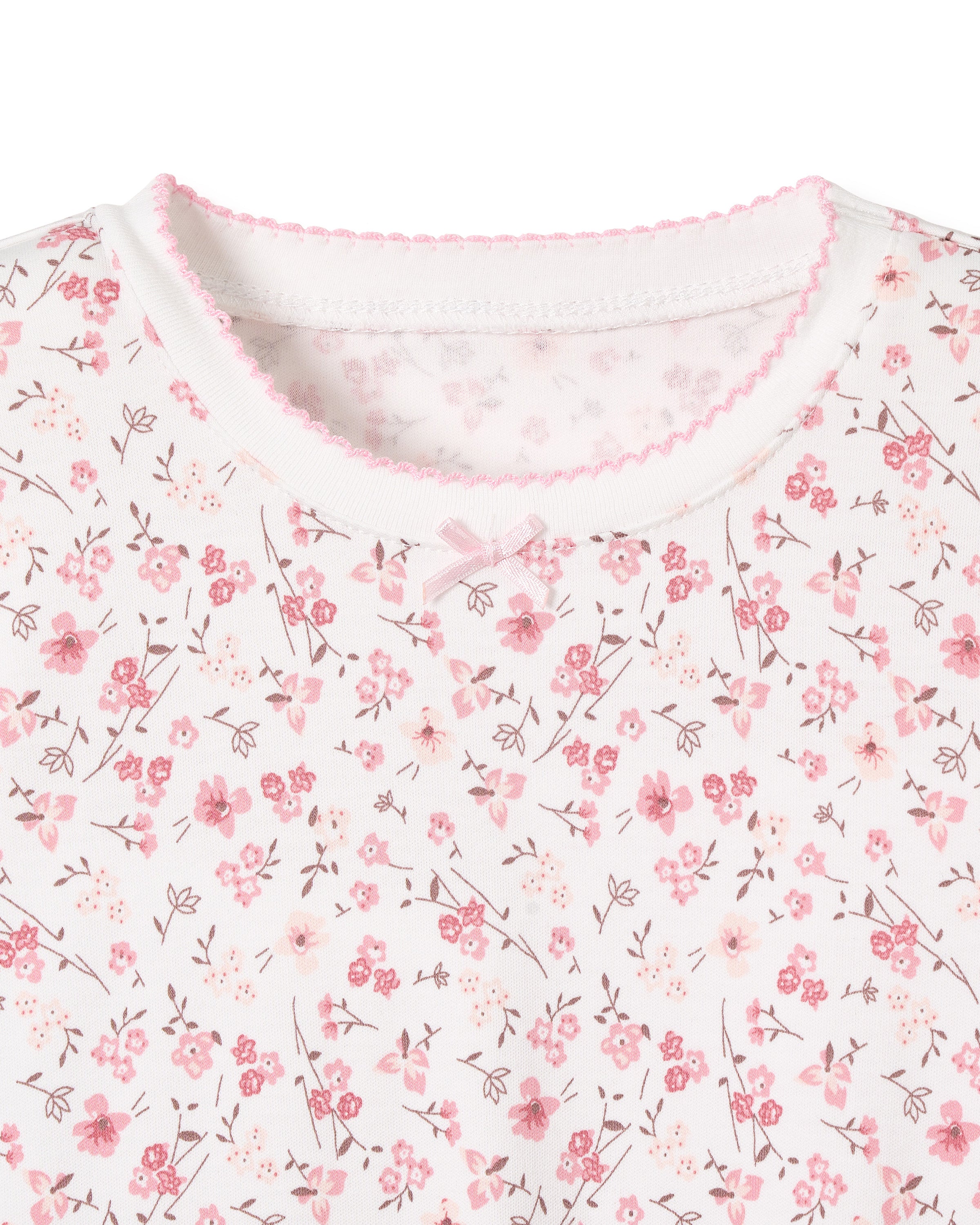 A close-up view showcases the white Pima Cotton fabric of Petite Plumes Kids Snug Fit Pajama Set in Dorset Floral, adorned with small pink flowers and leaves. The neckline features a pink scalloped trim, hinting at its cozy long sleeve top and pant design.