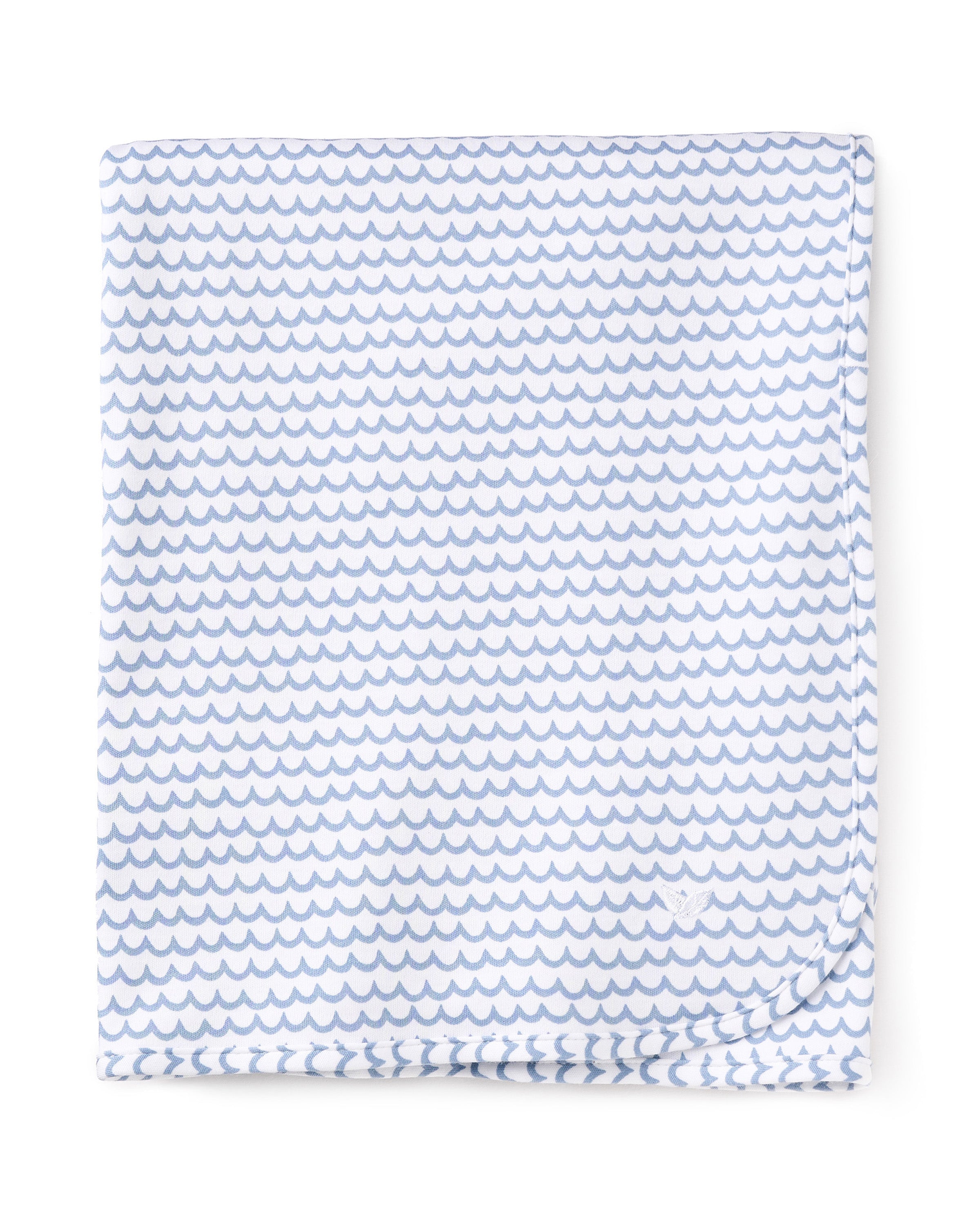 The Pima Baby Blanket in La Mer by Petite Plume is a folded white fabric, made from soft and cozy Peruvian Pima Cotton, adorned with small blue wave-like patterns and neatly finished edges.