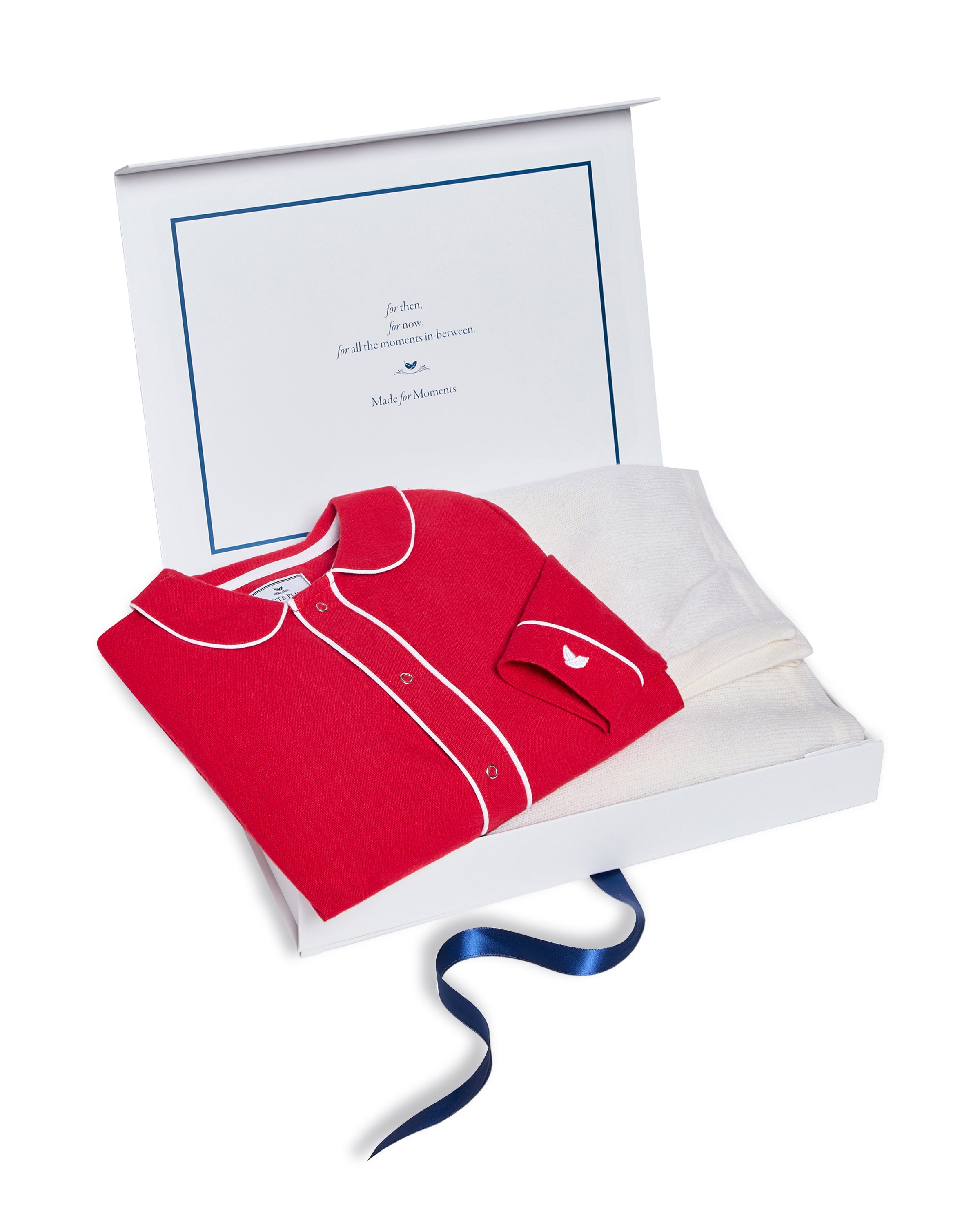 An open gift box showcases Petite Plumes Babys Flannel Cambridge Romper in red with white piping and a heart emblem, beside a luxurious cashmere blanket. The set is adorned with a blue ribbon and includes a heartfelt message inside.