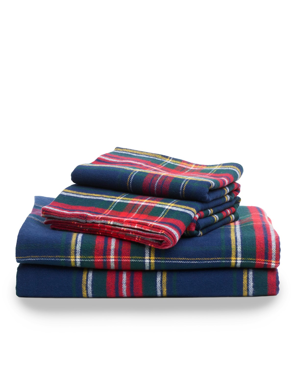 A folded stack of Petite Plumes Flannel Sheets in Windsor Tartan, featuring red, green, and yellow stripes on a navy background, sits against a white surface.